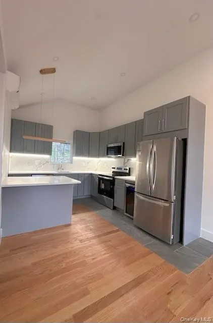 Kitchen with light wood-style floors, appliances with stainless steel finishes, decorative light fixtures, gray cabinets, and decorative backsplash Kitchen with light wood-style floors, appliances with stainless steel finishes, decorative light fixtures, gray cabinets, and decorative backsplash