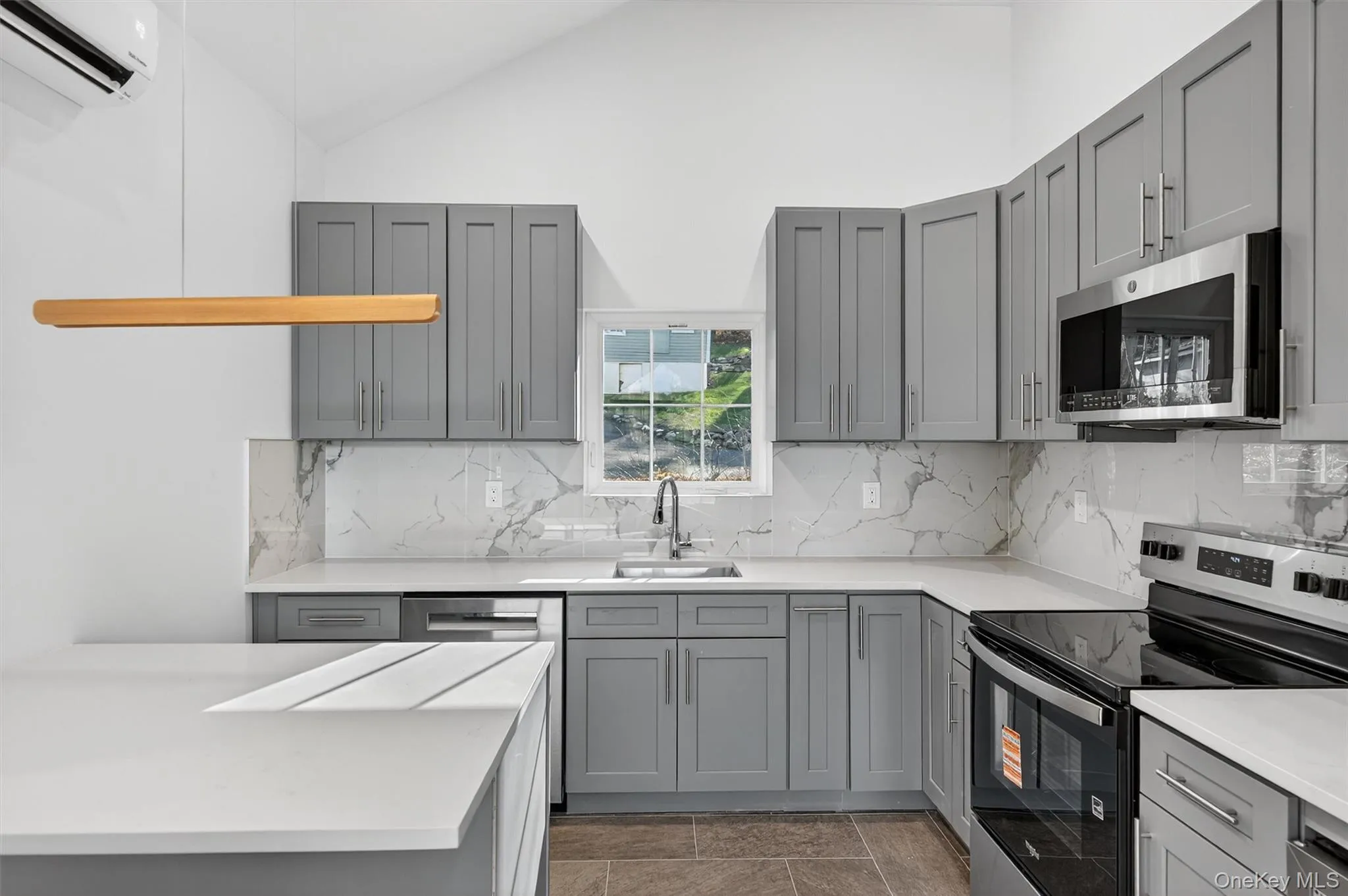 Kitchen featuring gray cabinetry, stainless steel appliances, vaulted ceiling, and a wall mounted AC Kitchen featuring gray cabinetry, stainless steel appliances, vaulted ceiling, and a wall mounted AC