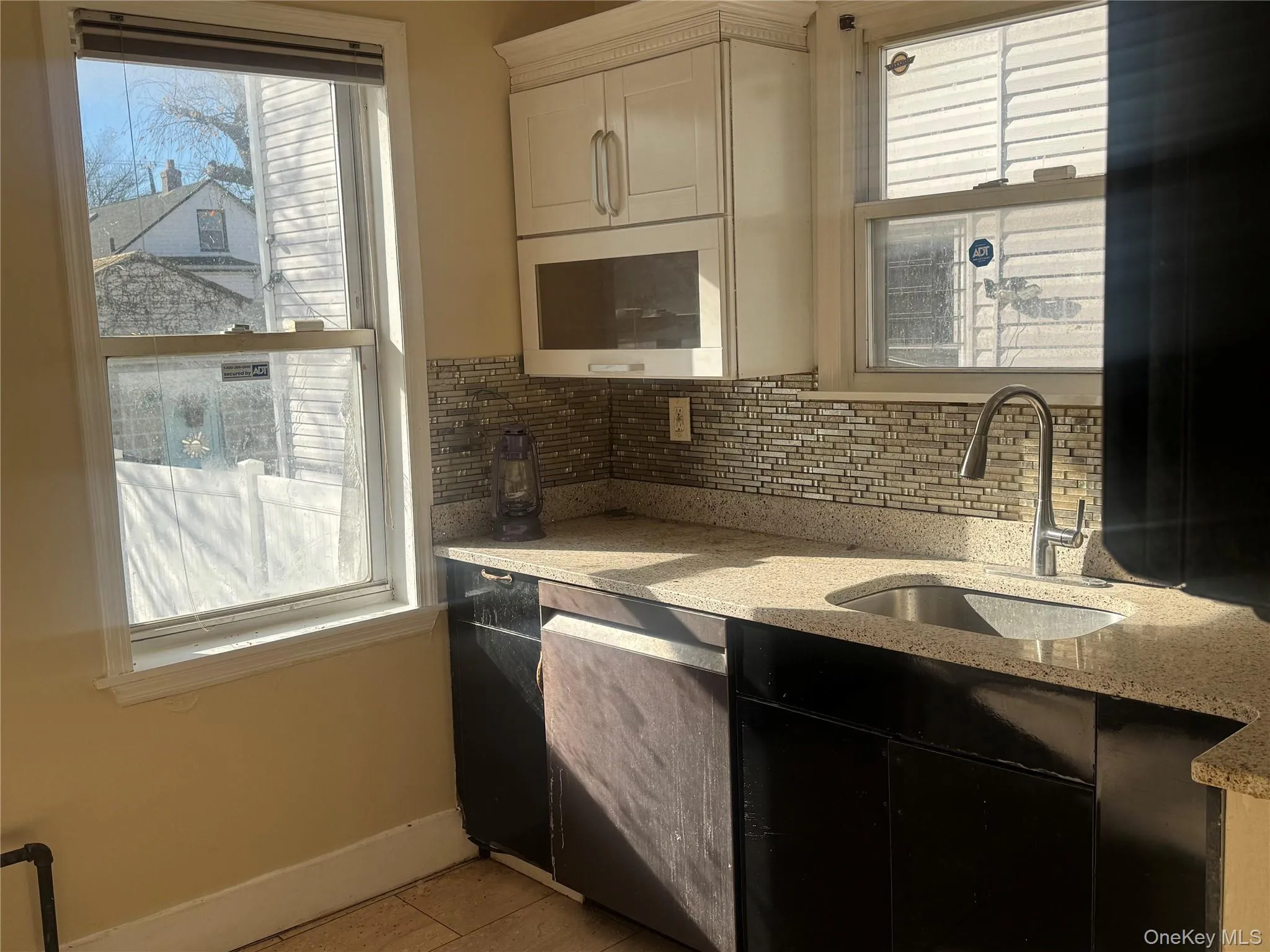 Kitchen with light stone countertops, stainless steel dishwasher, and decorative backsplash Kitchen with light stone countertops, stainless steel dishwasher, and decorative backsplash