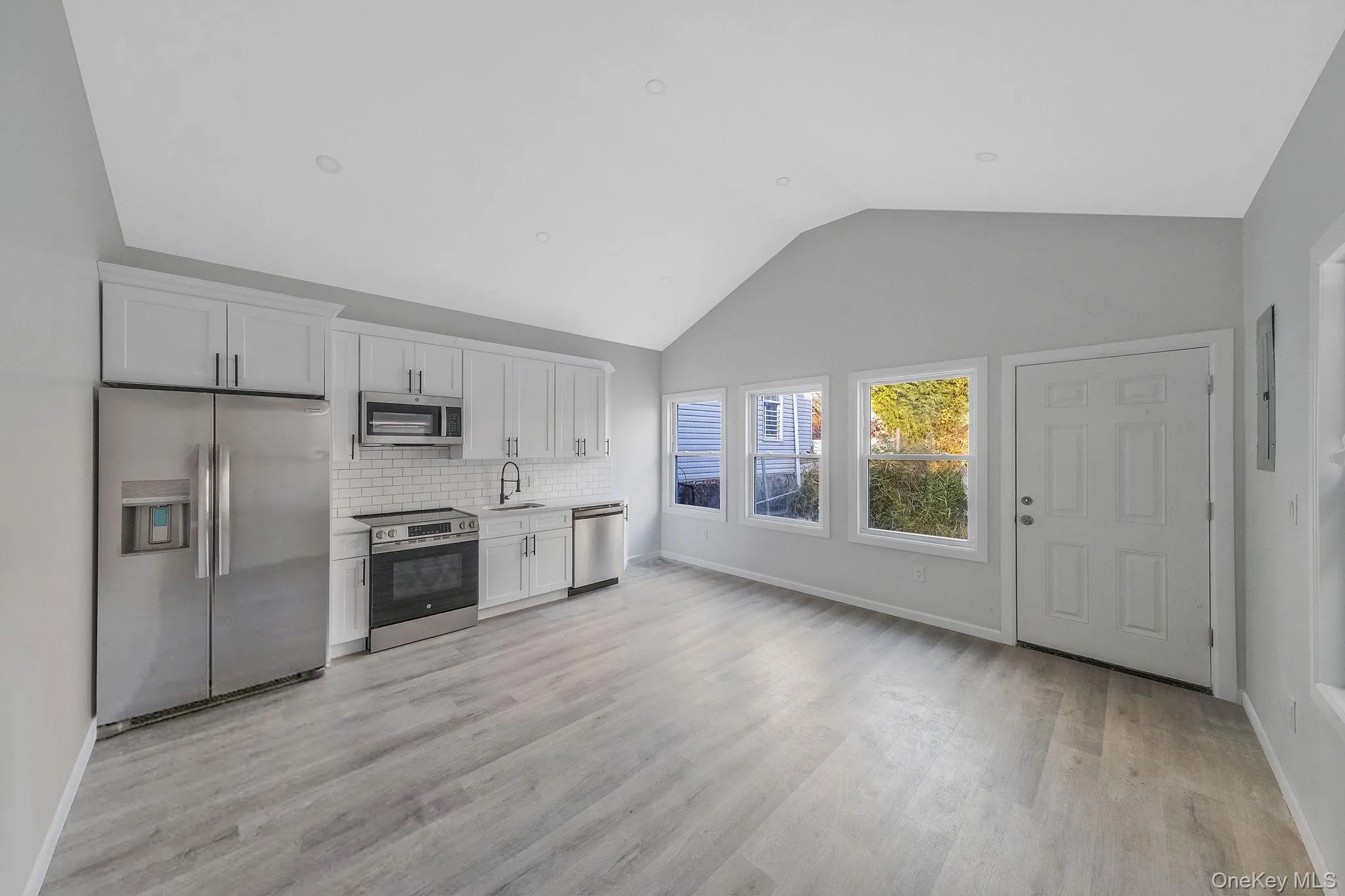 Kitchen with stainless steel appliances, white cabinetry, lofted ceiling, decorative backsplash, and light wood-style flooring Kitchen with stainless steel appliances, white cabinetry, lofted ceiling, decorative backsplash, and light wood-style flooring