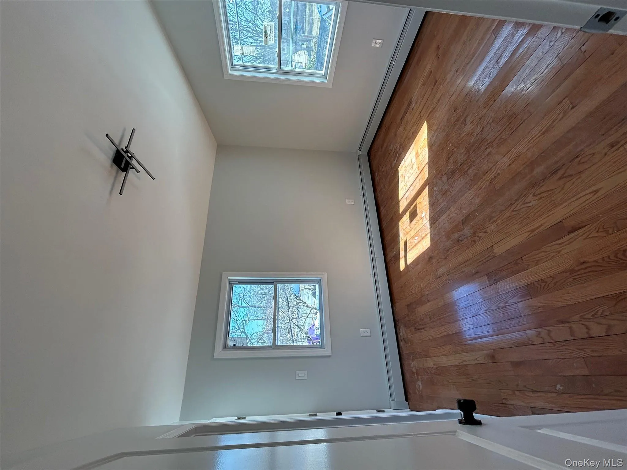 Unfurnished room featuring healthy amount of natural light, baseboard heating, and hardwood / wood-style flooring Unfurnished room featuring healthy amount of natural light, baseboard heating, and hardwood / wood-style flooring