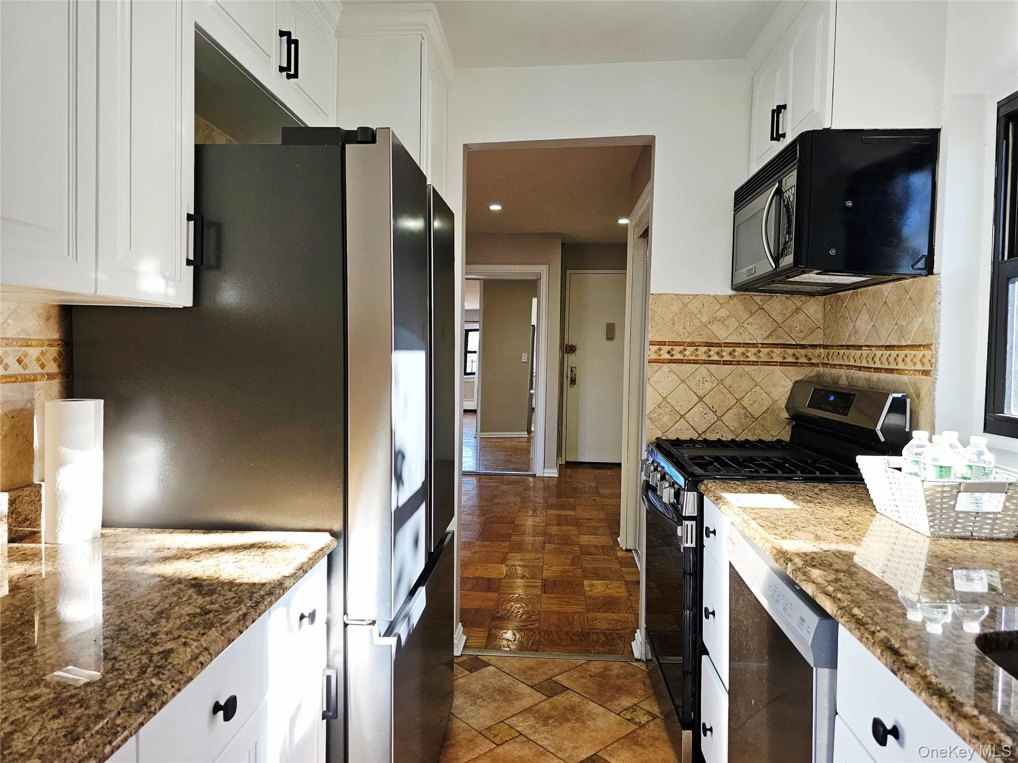 Kitchen featuring stainless steel appliances, dark stone counters, white cabinets, decorative backsplash, and stone tile flooring Kitchen featuring stainless steel appliances, dark stone counters, white cabinets, decorative backsplash, and stone tile flooring