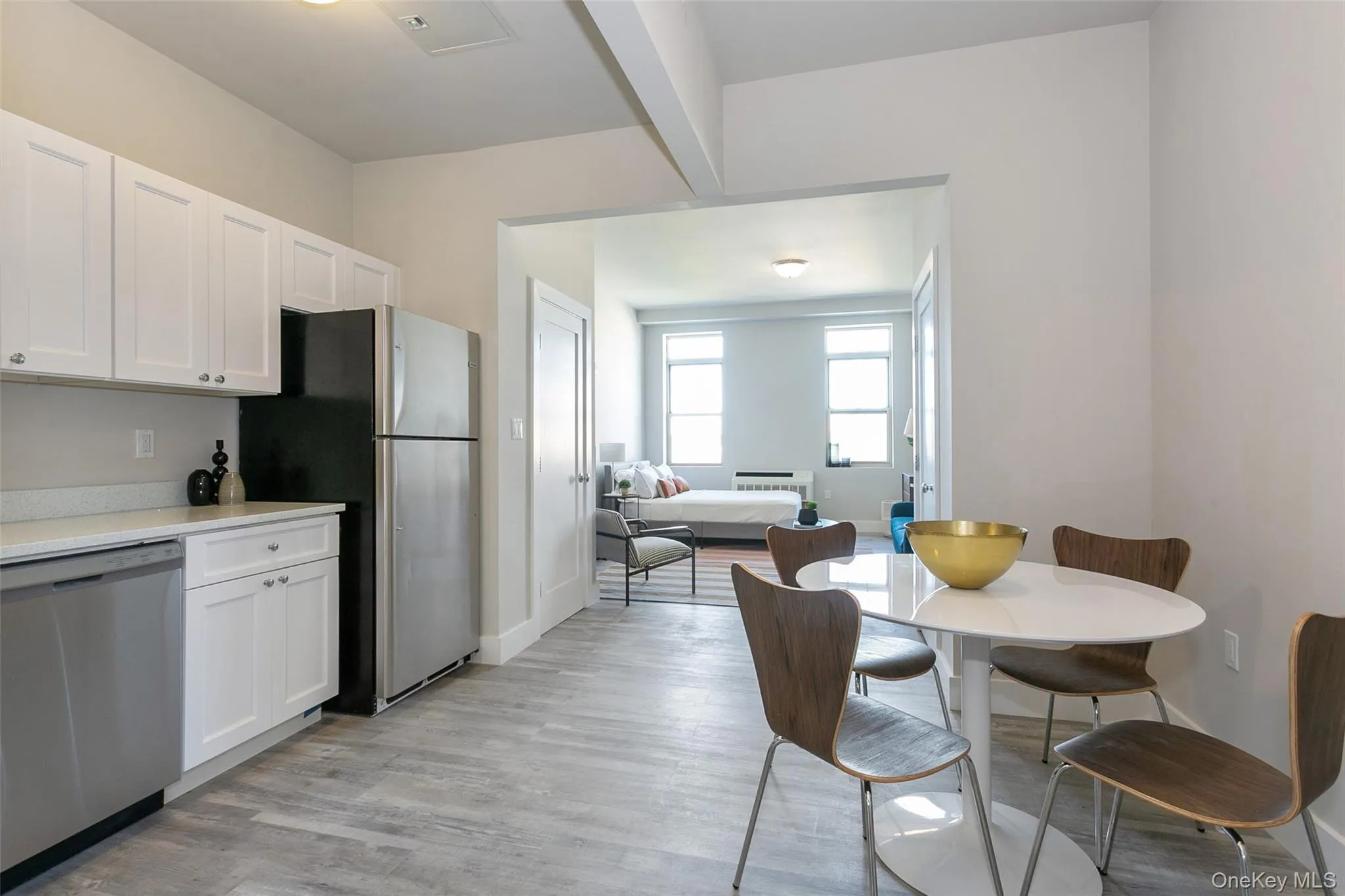 Kitchen featuring stainless steel appliances, white cabinets, beam ceiling, light wood-type flooring, and light stone countertops Kitchen featuring stainless steel appliances, white cabinets, beam ceiling, light wood-type flooring, and light stone countertops