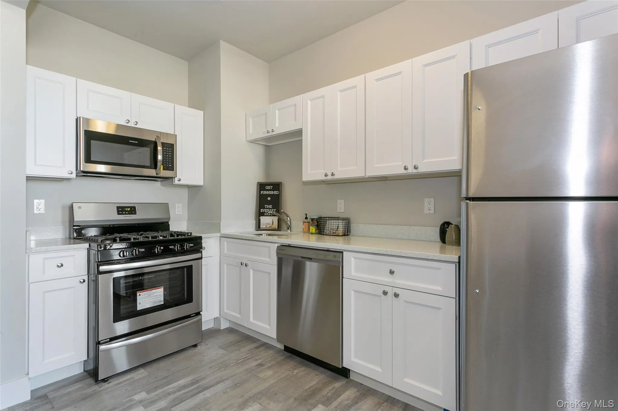 Kitchen with stainless steel appliances, white cabinetry, light wood-type flooring, and light stone countertops Kitchen with stainless steel appliances, white cabinetry, light wood-type flooring, and light stone countertops