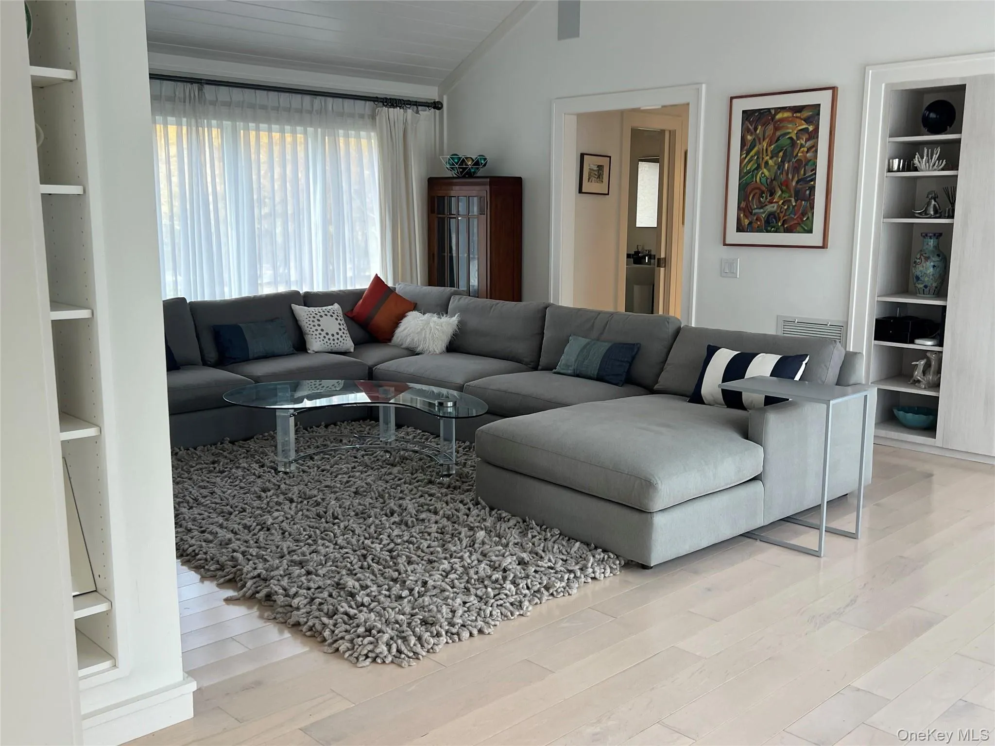 Living room with built in shelves, light wood-style flooring, and lofted ceiling Living room with built in shelves, light wood-style flooring, and lofted ceiling
