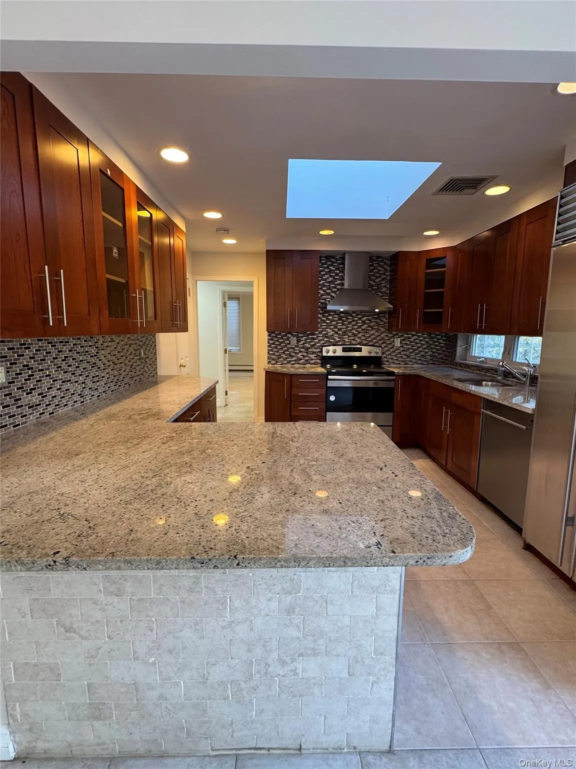 Kitchen with glass insert cabinets, appliances with stainless steel finishes, light stone counters, wall chimney exhaust hood, and recessed lighting Kitchen with glass insert cabinets, appliances with stainless steel finishes, light stone counters, wall chimney exhaust hood, and recessed lighting