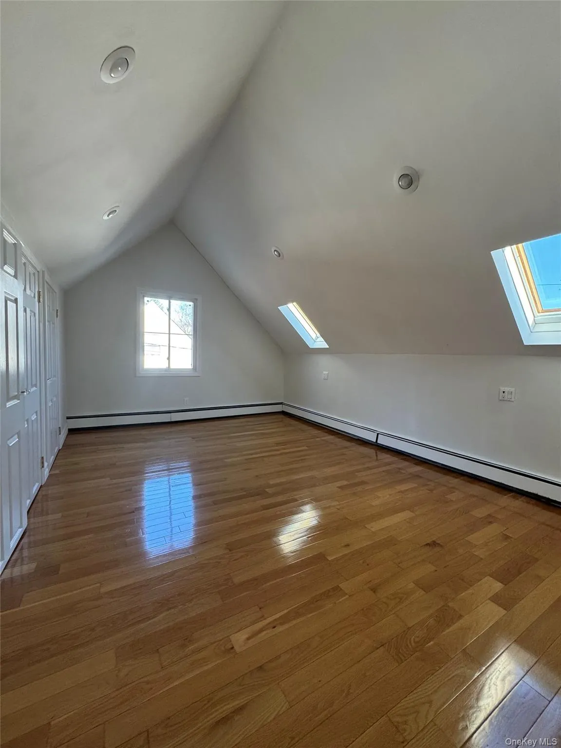 Additional living space featuring a skylight, lofted ceiling, baseboard heating, and hardwood / wood-style flooring Additional living space featuring a skylight, lofted ceiling, baseboard heating, and hardwood / wood-style flooring