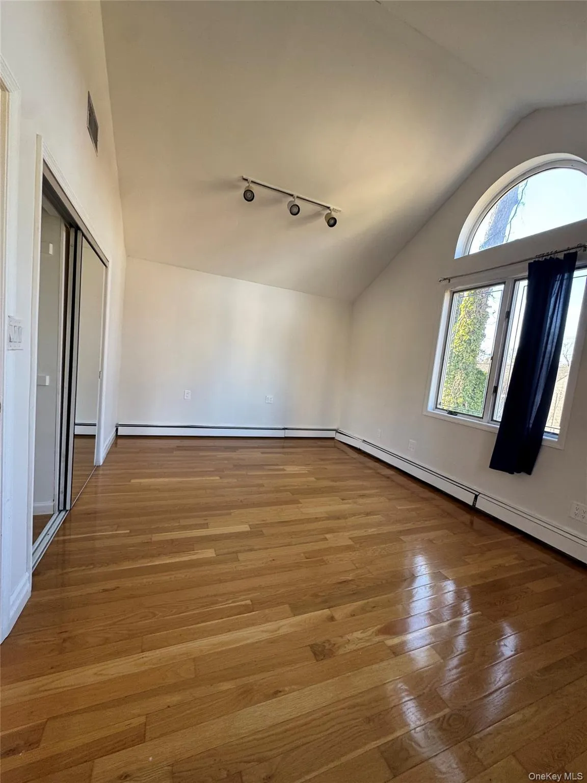 Unfurnished room with baseboard heating, light wood-type flooring, track lighting, and high vaulted ceiling Unfurnished room with baseboard heating, light wood-type flooring, track lighting, and high vaulted ceiling