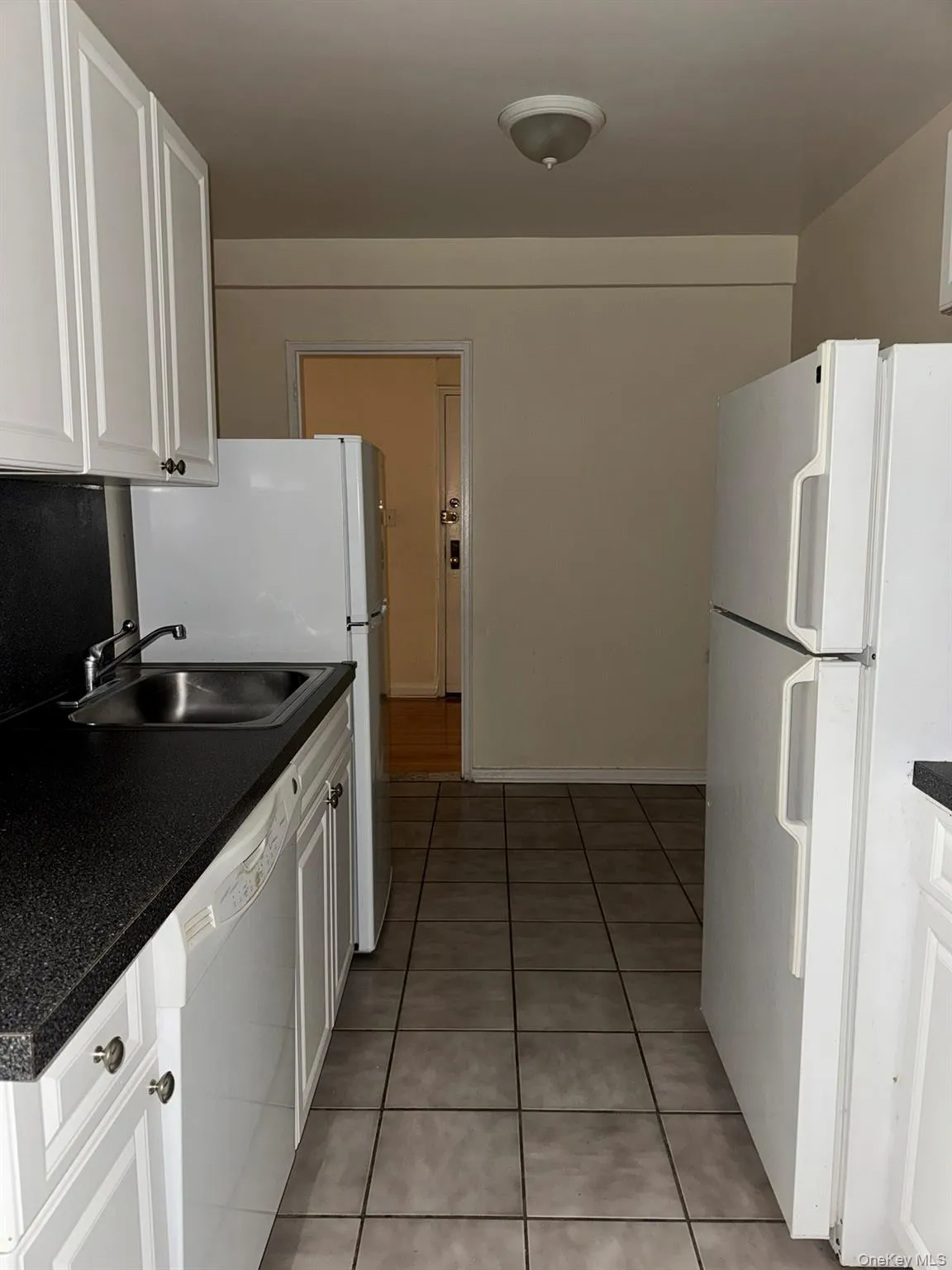 Kitchen featuring white appliances, white cabinetry, light tile patterned flooring, and dark countertops Kitchen featuring white appliances, white cabinetry, light tile patterned flooring, and dark countertops