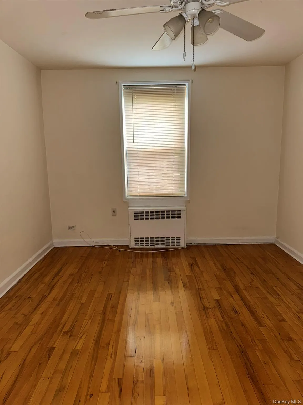 Empty room featuring radiator heating unit, hardwood / wood-style floors, and ceiling fan Empty room featuring radiator heating unit, hardwood / wood-style floors, and ceiling fan