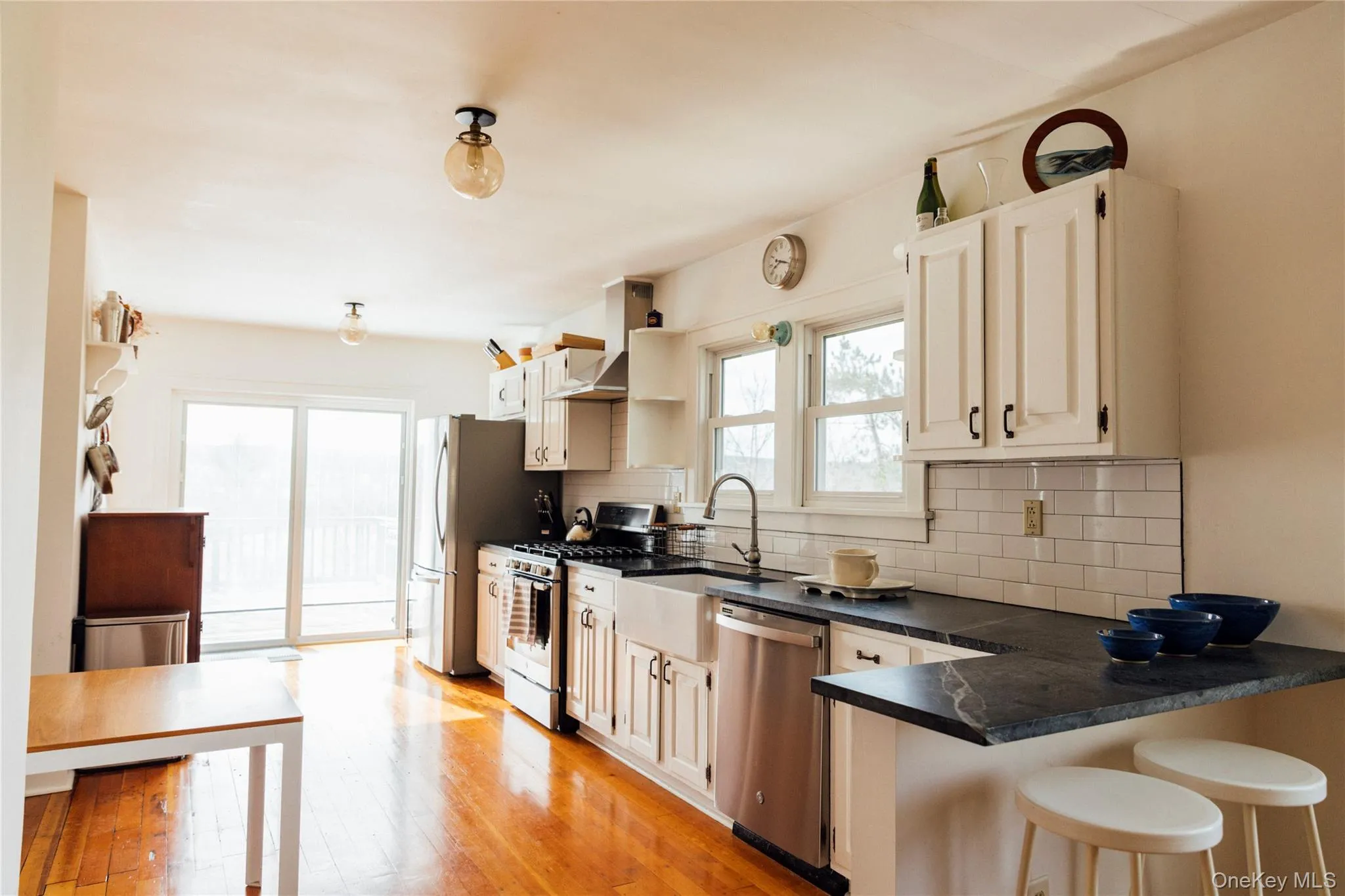 Kitchen featuring dark countertops, tasteful backsplash, a breakfast bar, stainless steel appliances, and wall chimney exhaust hood Kitchen featuring dark countertops, tasteful backsplash, a breakfast bar, stainless steel appliances, and wall chimney exhaust hood