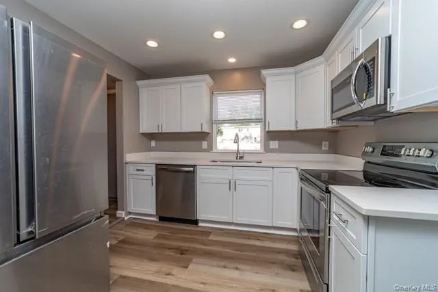 Kitchen with appliances with stainless steel finishes, white cabinets, light wood-style flooring, and recessed lighting Kitchen with appliances with stainless steel finishes, white cabinets, light wood-style flooring, and recessed lighting
