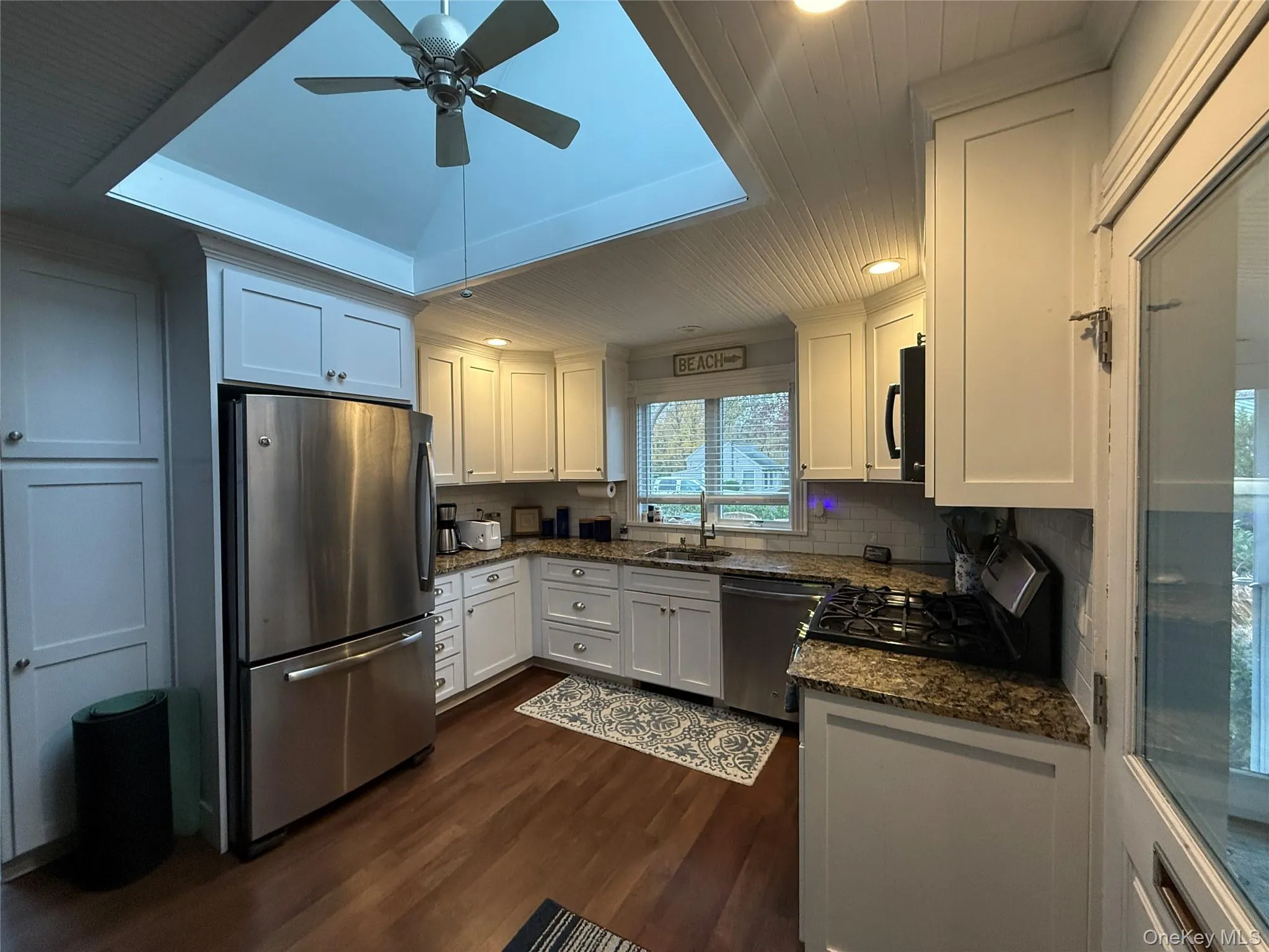 Kitchen with white cabinetry, stainless steel appliances, dark stone counters, dark wood-style floors, and recessed lighting Kitchen with white cabinetry, stainless steel appliances, dark stone counters, dark wood-style floors, and recessed lighting