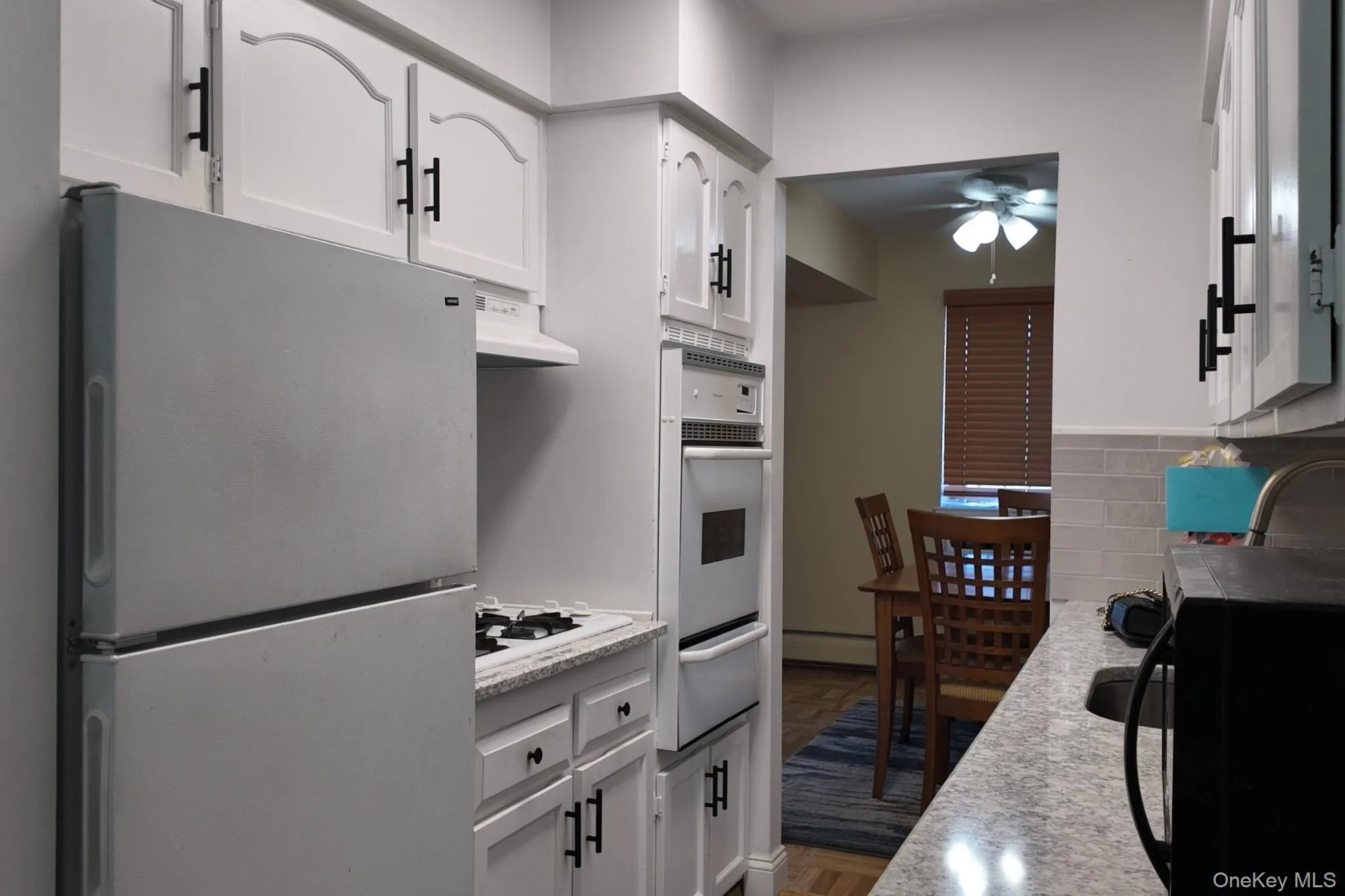 Kitchen featuring freestanding refrigerator, black microwave, white cabinetry, wall oven, and a ceiling fan Kitchen featuring freestanding refrigerator, black microwave, white cabinetry, wall oven, and a ceiling fan