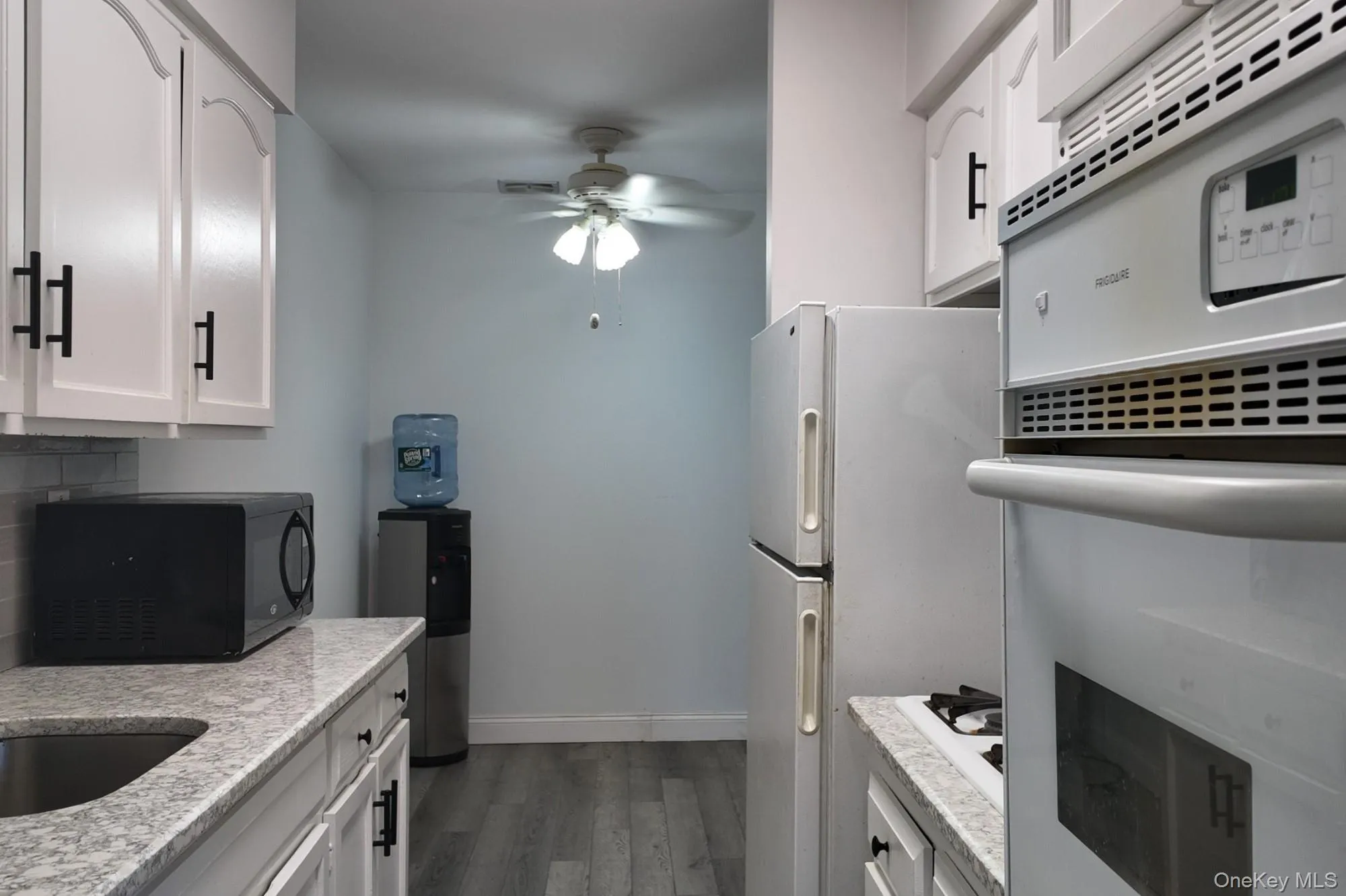 Kitchen with white appliances, white cabinetry, a ceiling fan, light stone counters, and dark wood finished floors Kitchen with white appliances, white cabinetry, a ceiling fan, light stone counters, and dark wood finished floors