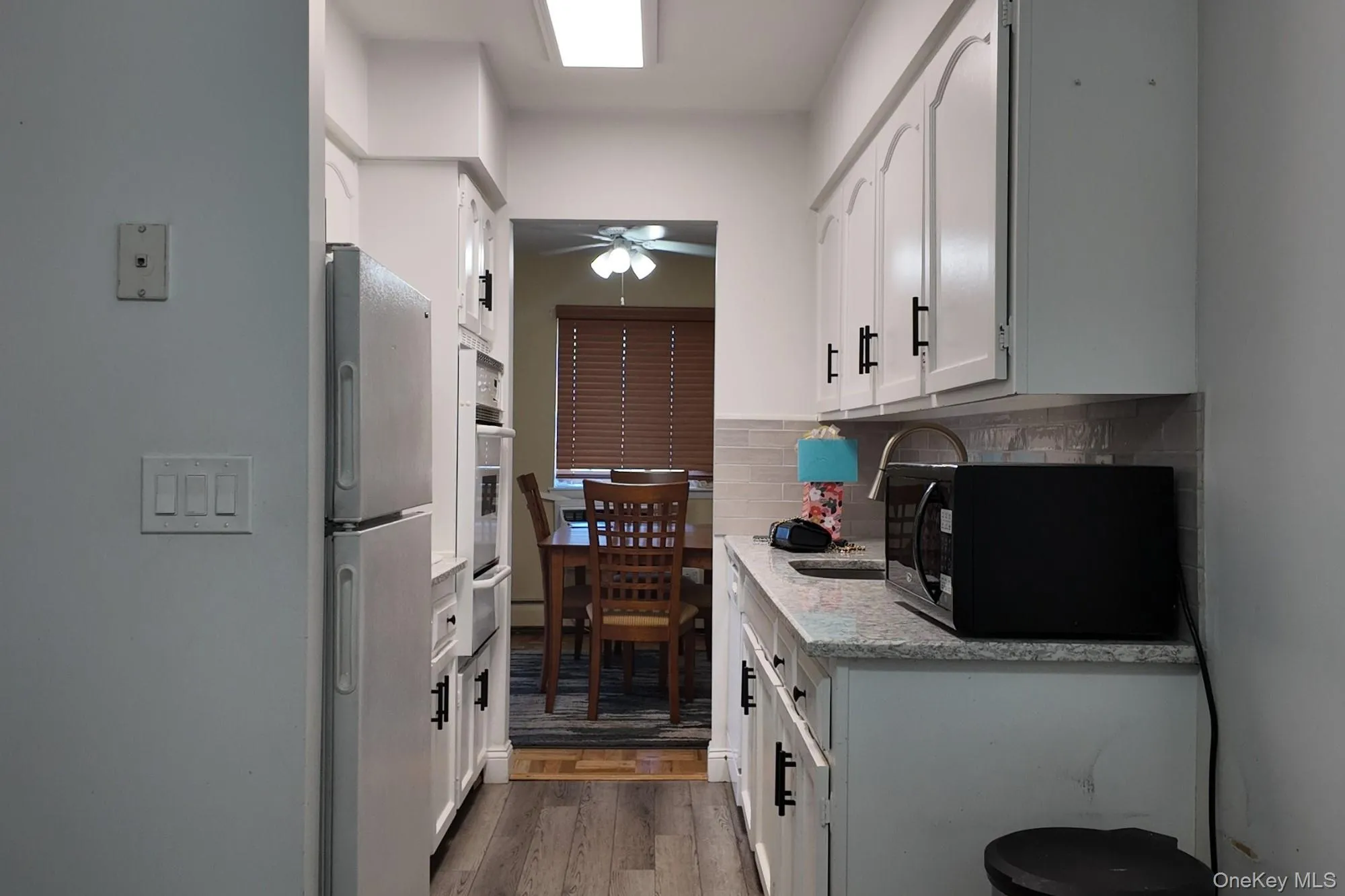 Kitchen featuring white cabinets, stainless steel appliances, dark wood finished floors, light stone counters, and tasteful backsplash Kitchen featuring white cabinets, stainless steel appliances, dark wood finished floors, light stone counters, and tasteful backsplash