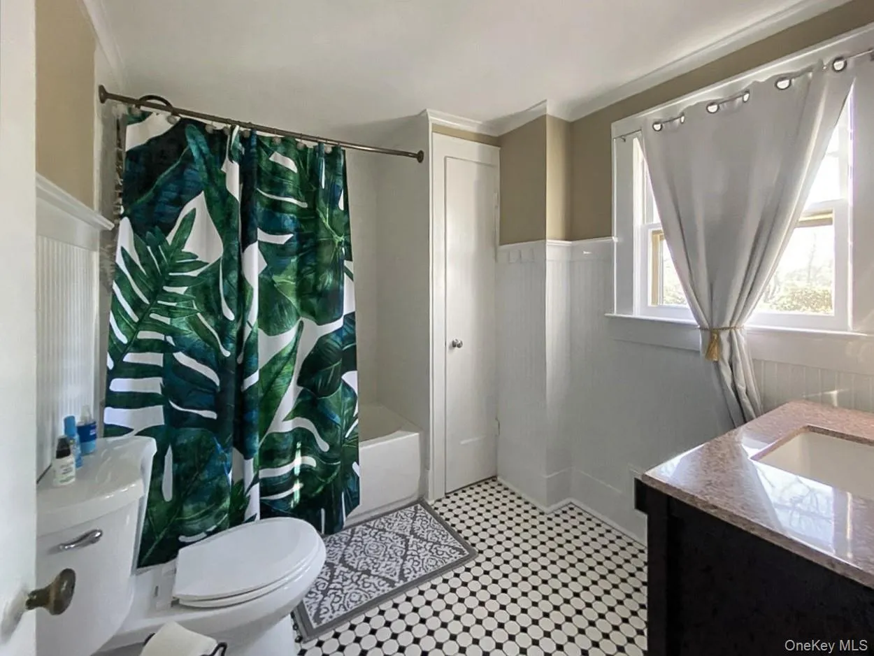 Bathroom featuring a wainscoted wall, vanity, shower / bath combo with shower curtain, light flooring, and ornamental molding Bathroom featuring a wainscoted wall, vanity, shower / bath combo with shower curtain, light flooring, and ornamental molding