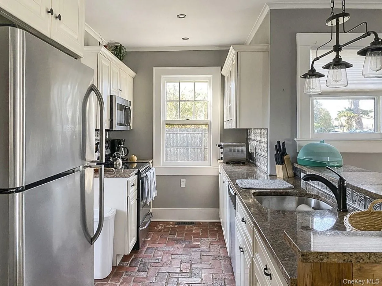 Kitchen featuring stainless steel appliances, white cabinets, brick floors, dark stone counters, and crown molding Kitchen featuring stainless steel appliances, white cabinets, brick floors, dark stone counters, and crown molding
