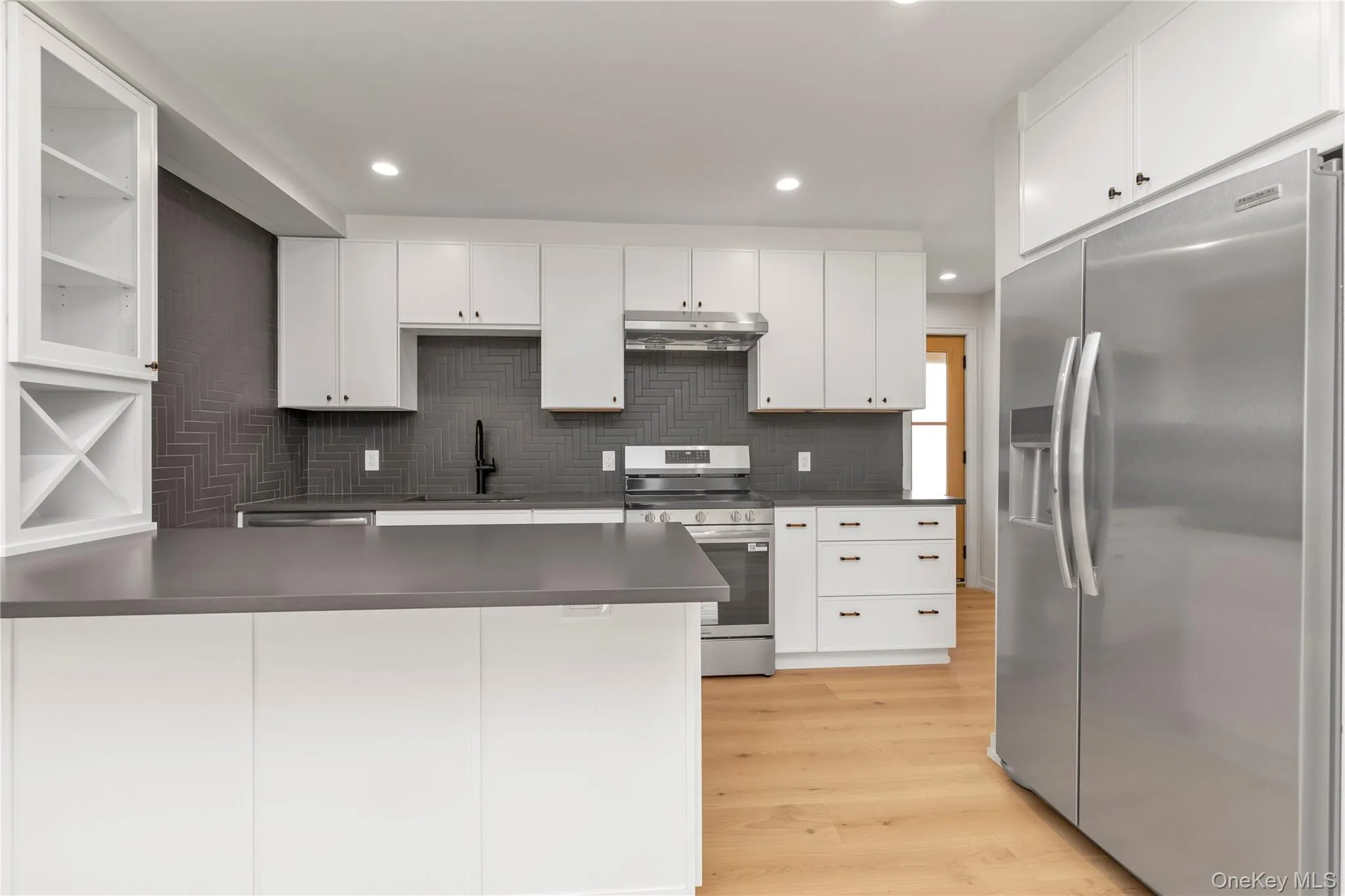 Kitchen with stainless steel appliances, a peninsula, white cabinetry, light wood finished floors, and recessed lighting Kitchen with stainless steel appliances, a peninsula, white cabinetry, light wood finished floors, and recessed lighting