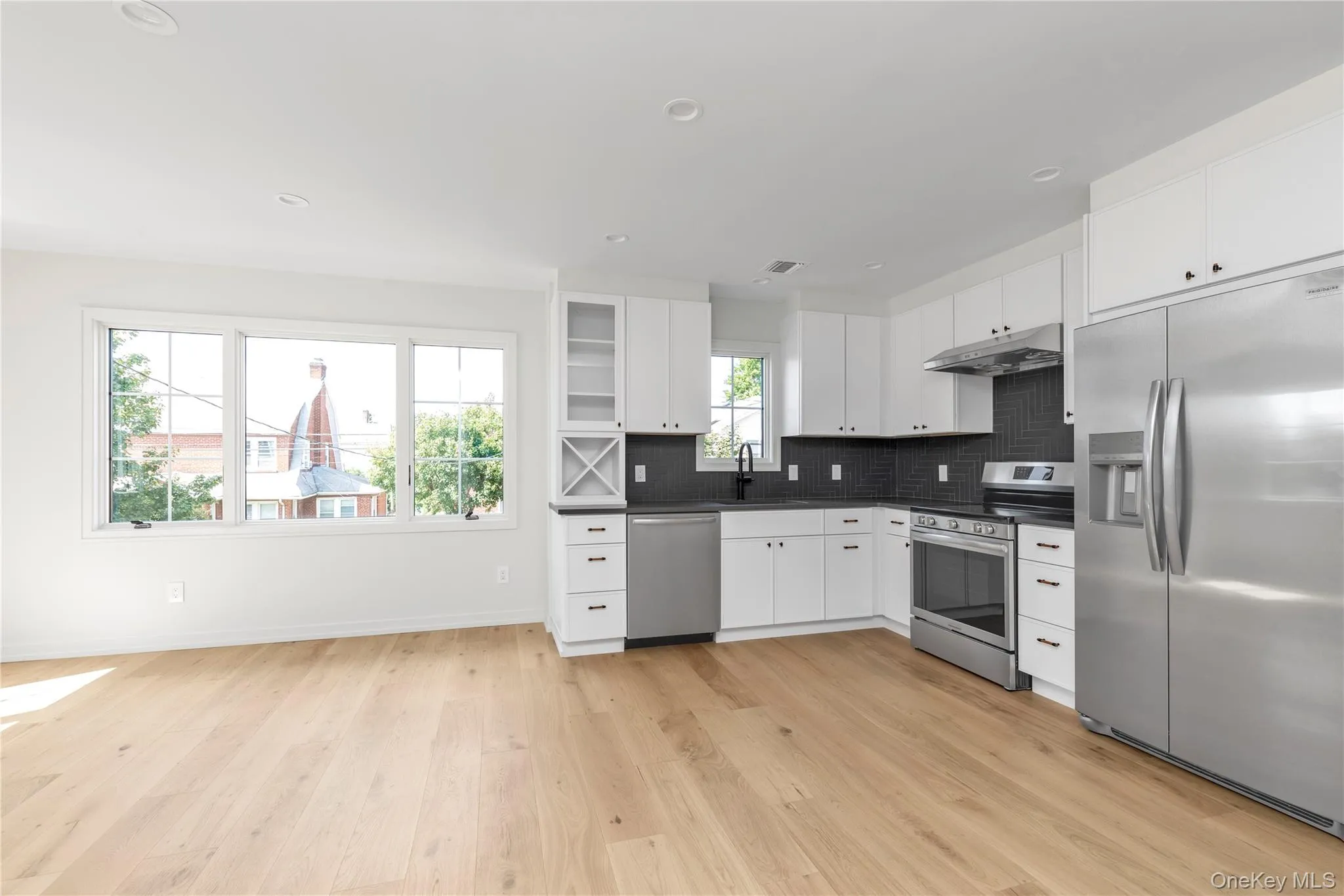 Kitchen with appliances with stainless steel finishes, white cabinets, decorative backsplash, dark countertops, and under cabinet range hood Kitchen with appliances with stainless steel finishes, white cabinets, decorative backsplash, dark countertops, and under cabinet range hood