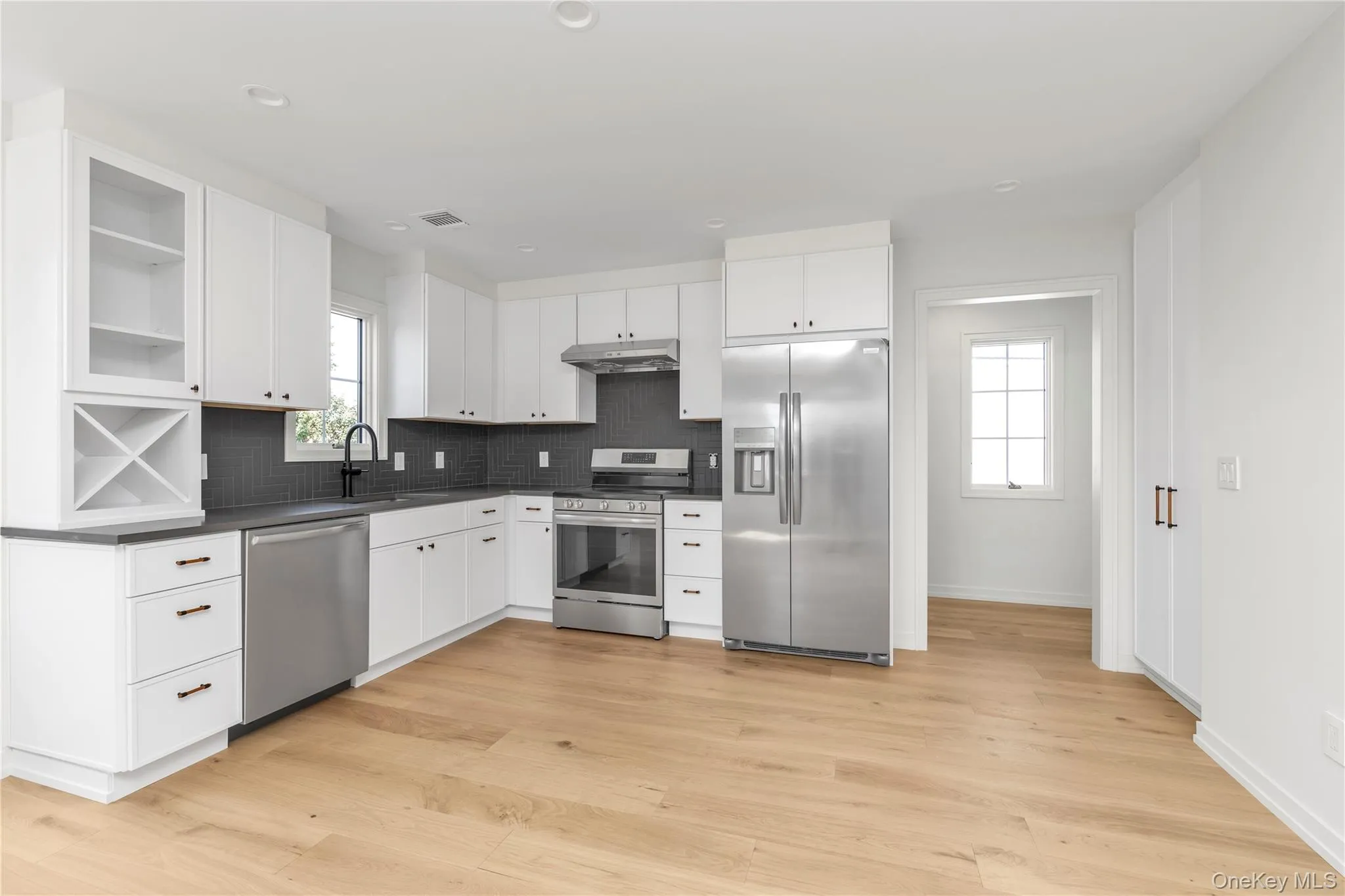 Kitchen featuring white cabinetry, stainless steel appliances, open shelves, dark countertops, and backsplash Kitchen featuring white cabinetry, stainless steel appliances, open shelves, dark countertops, and backsplash