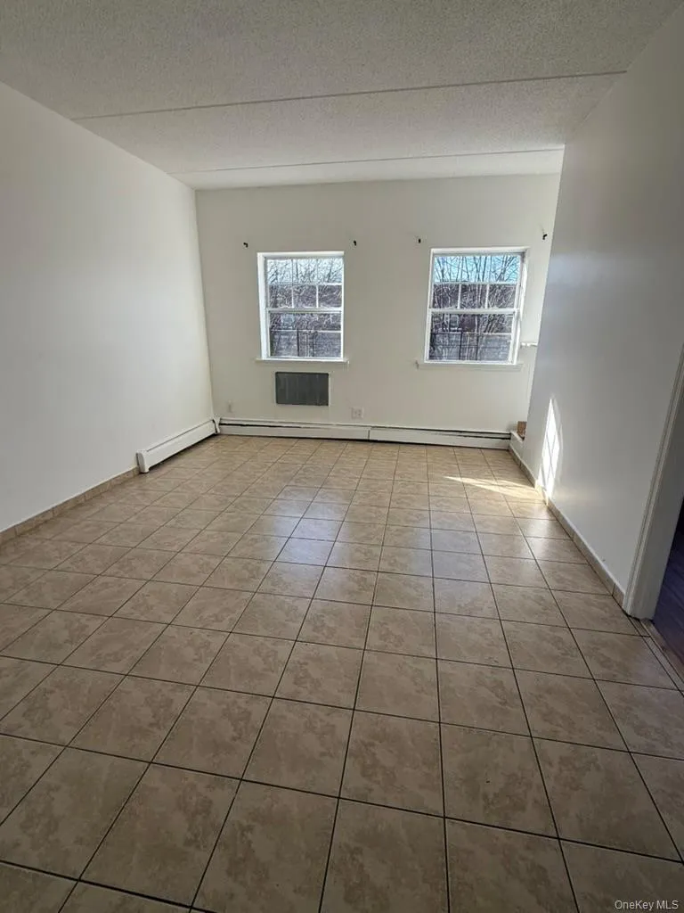 Empty room with tile patterned floors, a textured ceiling, and a baseboard radiator Empty room with tile patterned floors, a textured ceiling, and a baseboard radiator