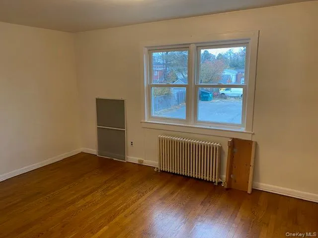 Unfurnished room featuring radiator and hardwood / wood-style flooring Unfurnished room featuring radiator and hardwood / wood-style flooring