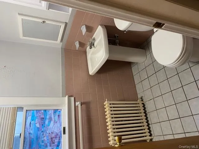 Bathroom featuring radiator heating unit, light tile patterned floors, a wainscoted wall, and tile walls Bathroom featuring radiator heating unit, light tile patterned floors, a wainscoted wall, and tile walls