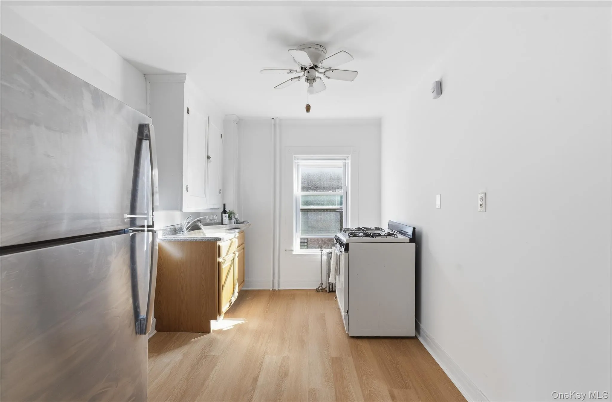 Kitchen featuring freestanding refrigerator, white gas range oven, light wood-type flooring, ceiling fan, and white cabinetry Kitchen featuring freestanding refrigerator, white gas range oven, light wood-type flooring, ceiling fan, and white cabinetry