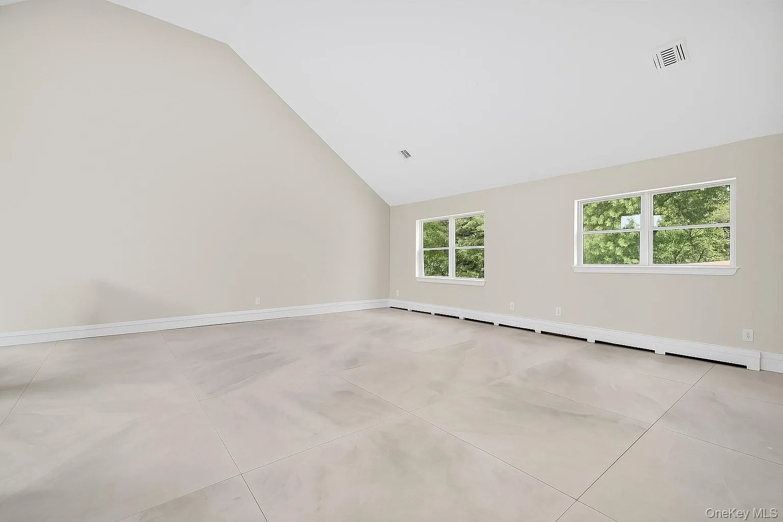 Empty room with a baseboard heating unit, high vaulted ceiling, and light tile patterned floors Empty room with a baseboard heating unit, high vaulted ceiling, and light tile patterned floors