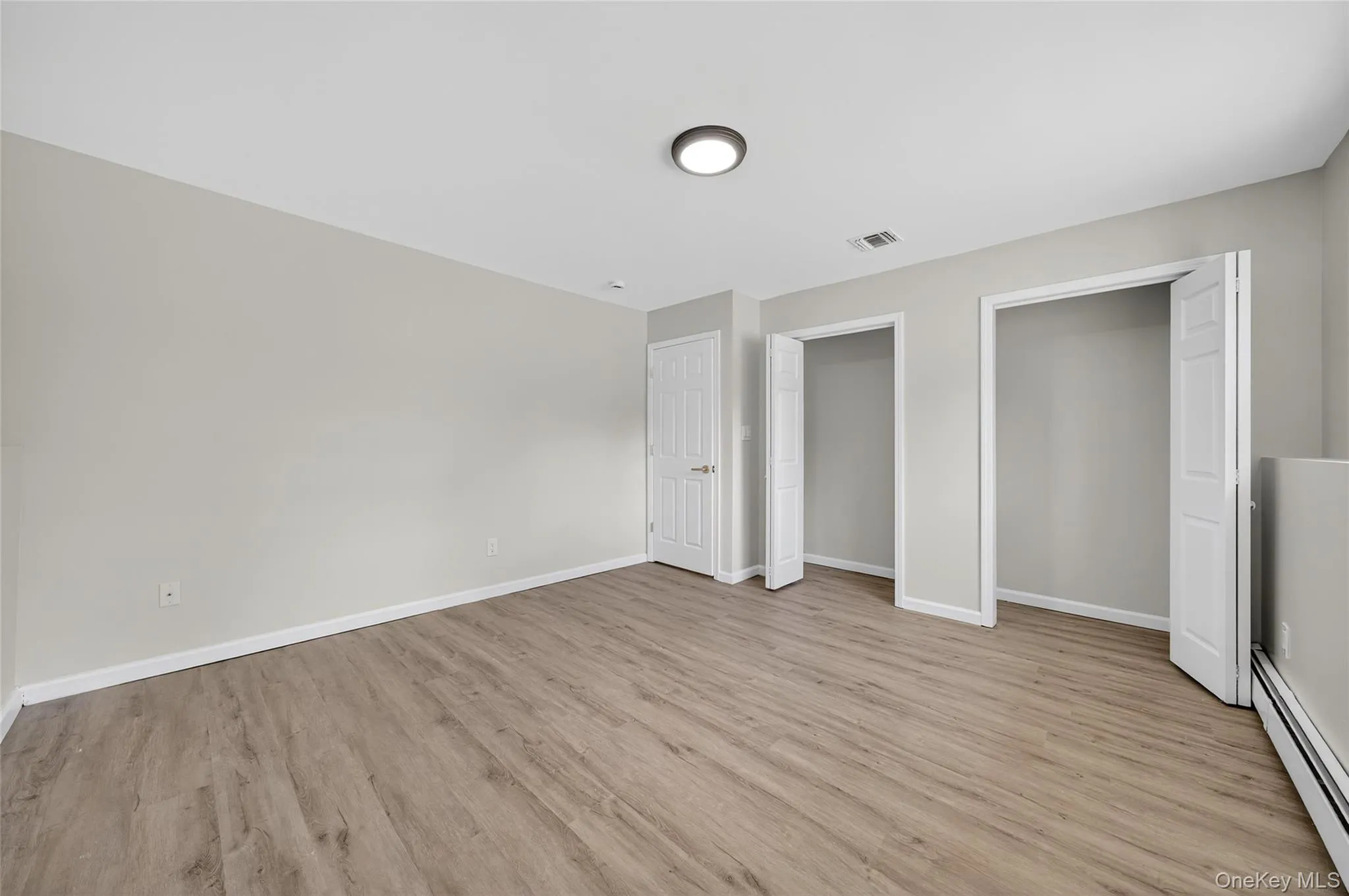 Unfurnished bedroom featuring a baseboard heating unit, multiple closets, and light wood-type flooring Unfurnished bedroom featuring a baseboard heating unit, multiple closets, and light wood-type flooring
