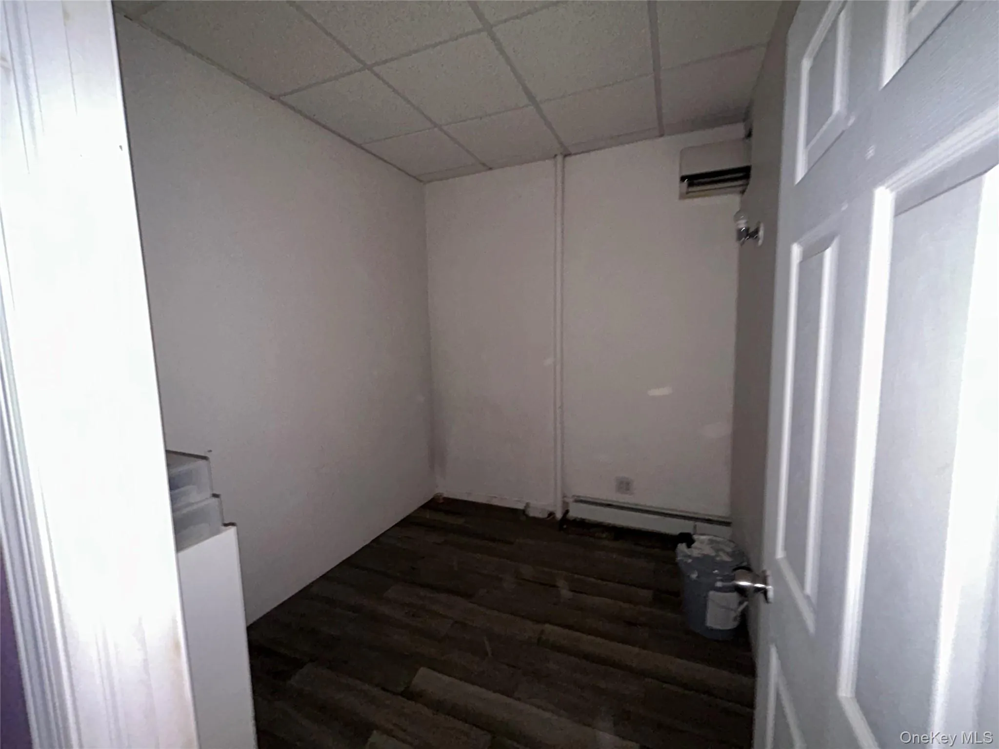 Spare room featuring a paneled ceiling, dark wood-style floors, a wall mounted air conditioner, and baseboard heating Spare room featuring a paneled ceiling, dark wood-style floors, a wall mounted air conditioner, and baseboard heating