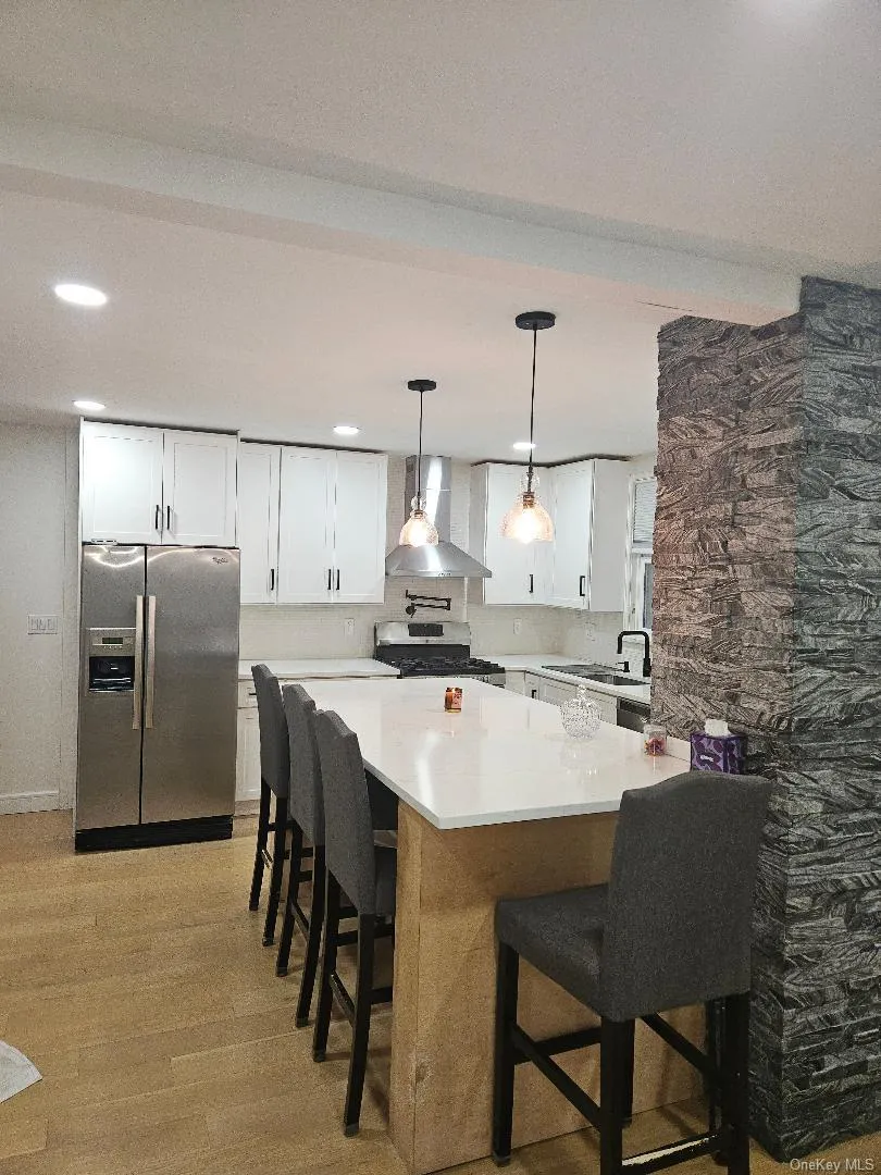 Kitchen with white cabinets, a kitchen bar, appliances with stainless steel finishes, hanging light fixtures, and recessed lighting Kitchen with white cabinets, a kitchen bar, appliances with stainless steel finishes, hanging light fixtures, and recessed lighting
