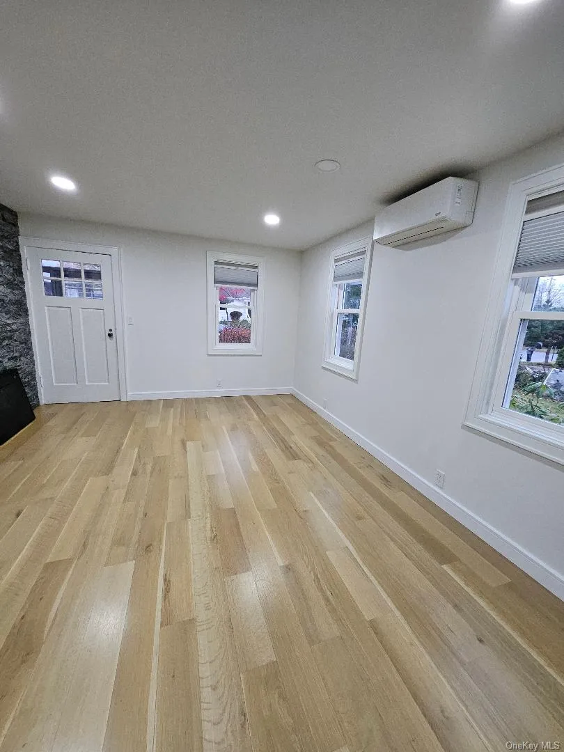 Below grade area with light wood-style floors, healthy amount of natural light, recessed lighting, and a wall mounted air conditioner Below grade area with light wood-style floors, healthy amount of natural light, recessed lighting, and a wall mounted air conditioner