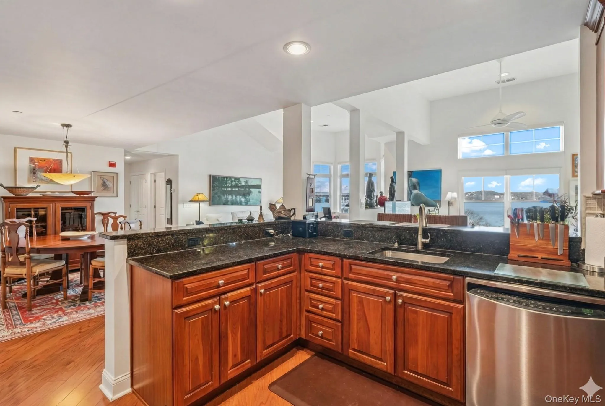 Kitchen with dishwasher, decorative light fixtures, brown cabinetry, light wood-style floors, and dark stone countertops Kitchen with dishwasher, decorative light fixtures, brown cabinetry, light wood-style floors, and dark stone countertops