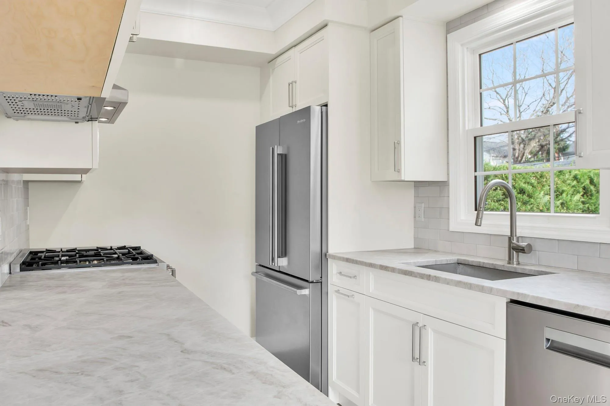 Renovated Kitchen with white cabinets, stainless steel appliances, light stone countertops, decorative backsplash, and extractor fan Renovated Kitchen with white cabinets, stainless steel appliances, light stone countertops, decorative backsplash, and extractor fan