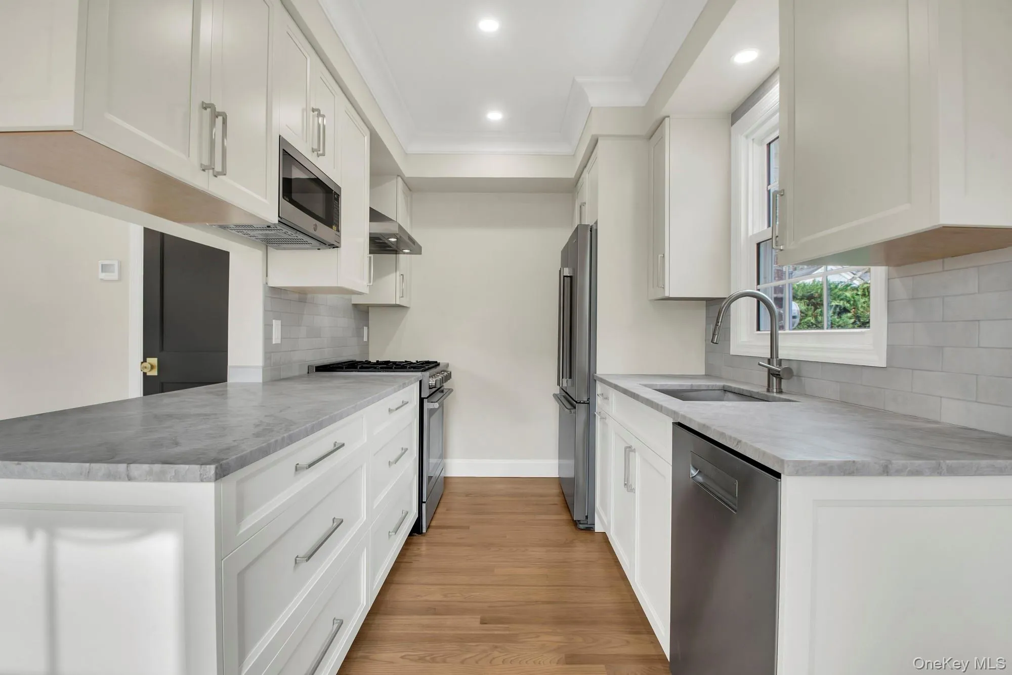 Renovated Kitchen featuring appliances with stainless steel finishes, white cabinetry, tasteful backsplash, extractor fan, and light wood-style flooring Renovated Kitchen featuring appliances with stainless steel finishes, white cabinetry, tasteful backsplash, extractor fan, and light wood-style flooring