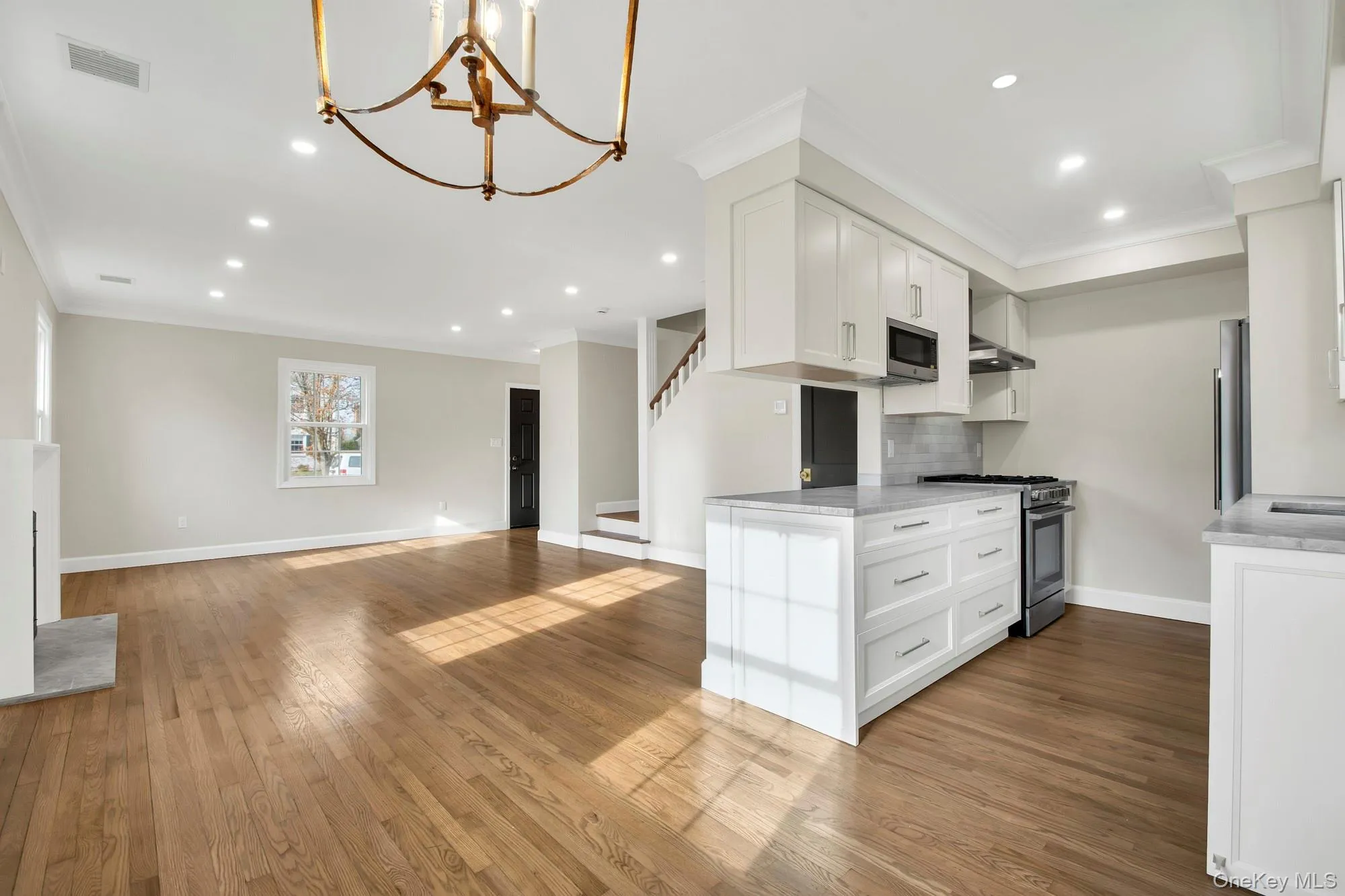 Open Kitchen featuring white cabinetry, appliances with stainless steel finishes, dark wood-style floors, a chandelier, and ornamental molding Open Kitchen featuring white cabinetry, appliances with stainless steel finishes, dark wood-style floors, a chandelier, and ornamental molding