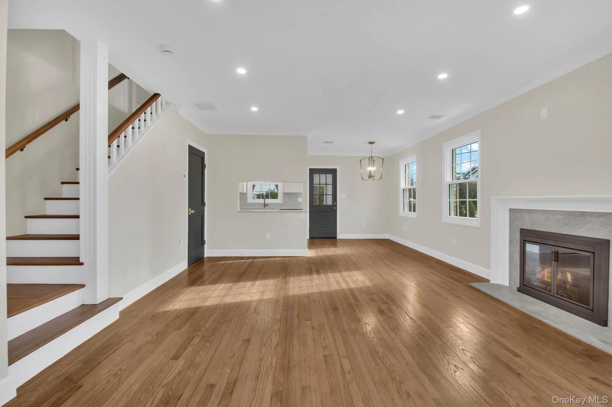 Open/ Bright living room featuring recessed lighting, ornamental molding, hardwood / wood-style flooring, a premium fireplace, and stairway Open/ Bright living room featuring recessed lighting, ornamental molding, hardwood / wood-style flooring, a premium fireplace, and stairway
