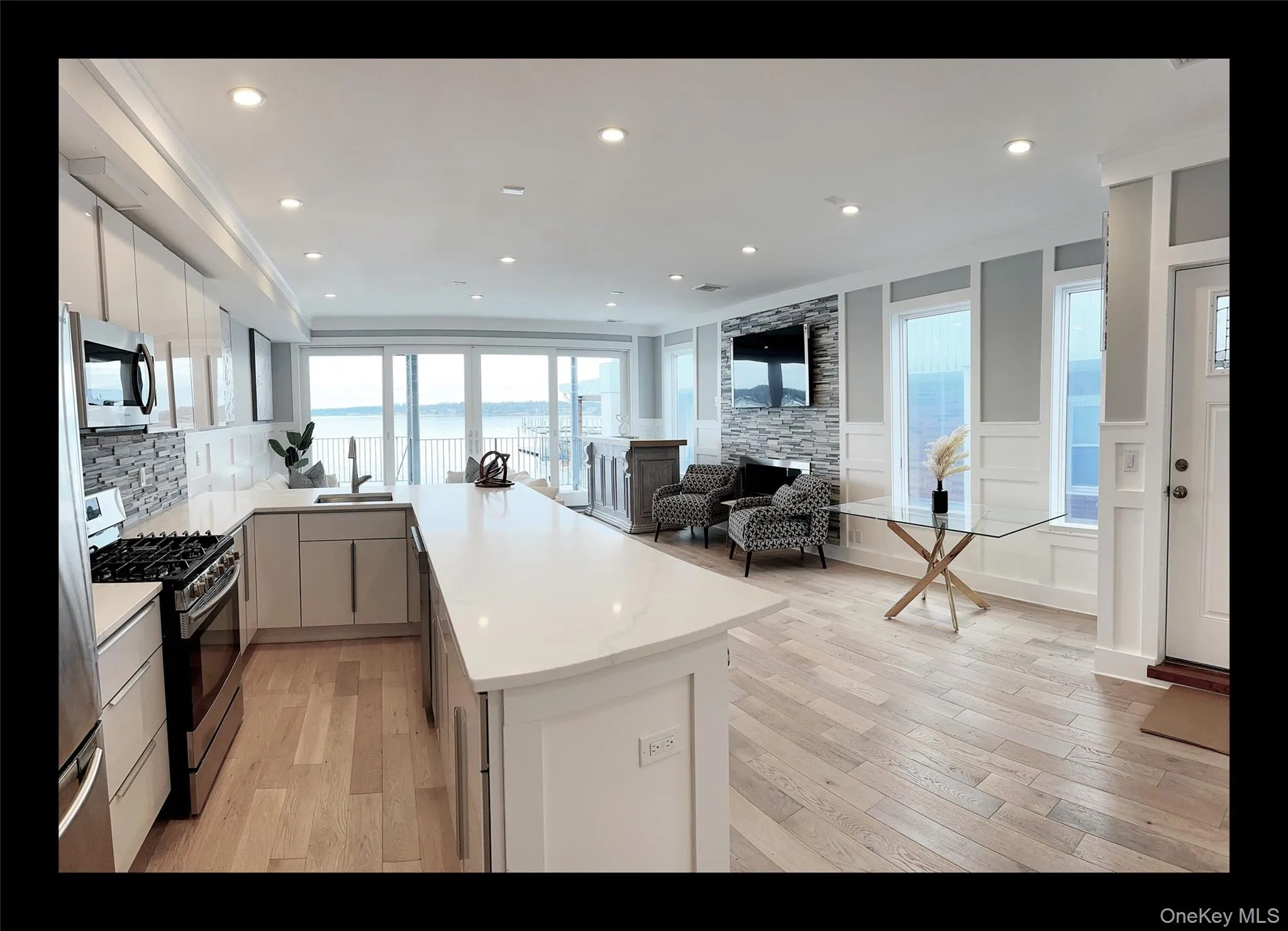 Kitchen featuring appliances with stainless steel finishes, a peninsula, light wood-style floors, a decorative wall, and modern cabinets Kitchen featuring appliances with stainless steel finishes, a peninsula, light wood-style floors, a decorative wall, and modern cabinets