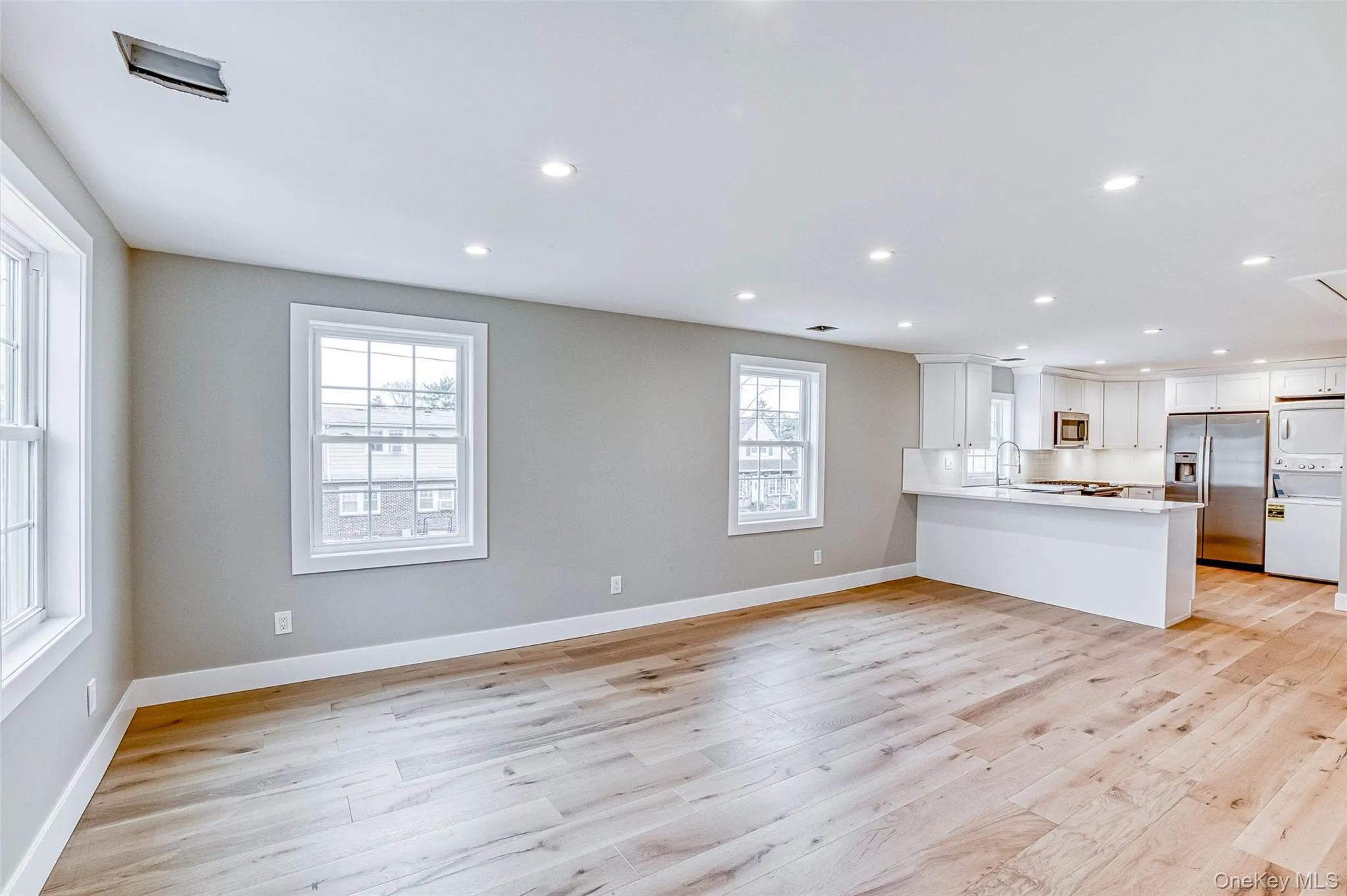 Unfurnished living room featuring stacked washer / dryer, light wood-style floors, and recessed lighting Unfurnished living room featuring stacked washer / dryer, light wood-style floors, and recessed lighting