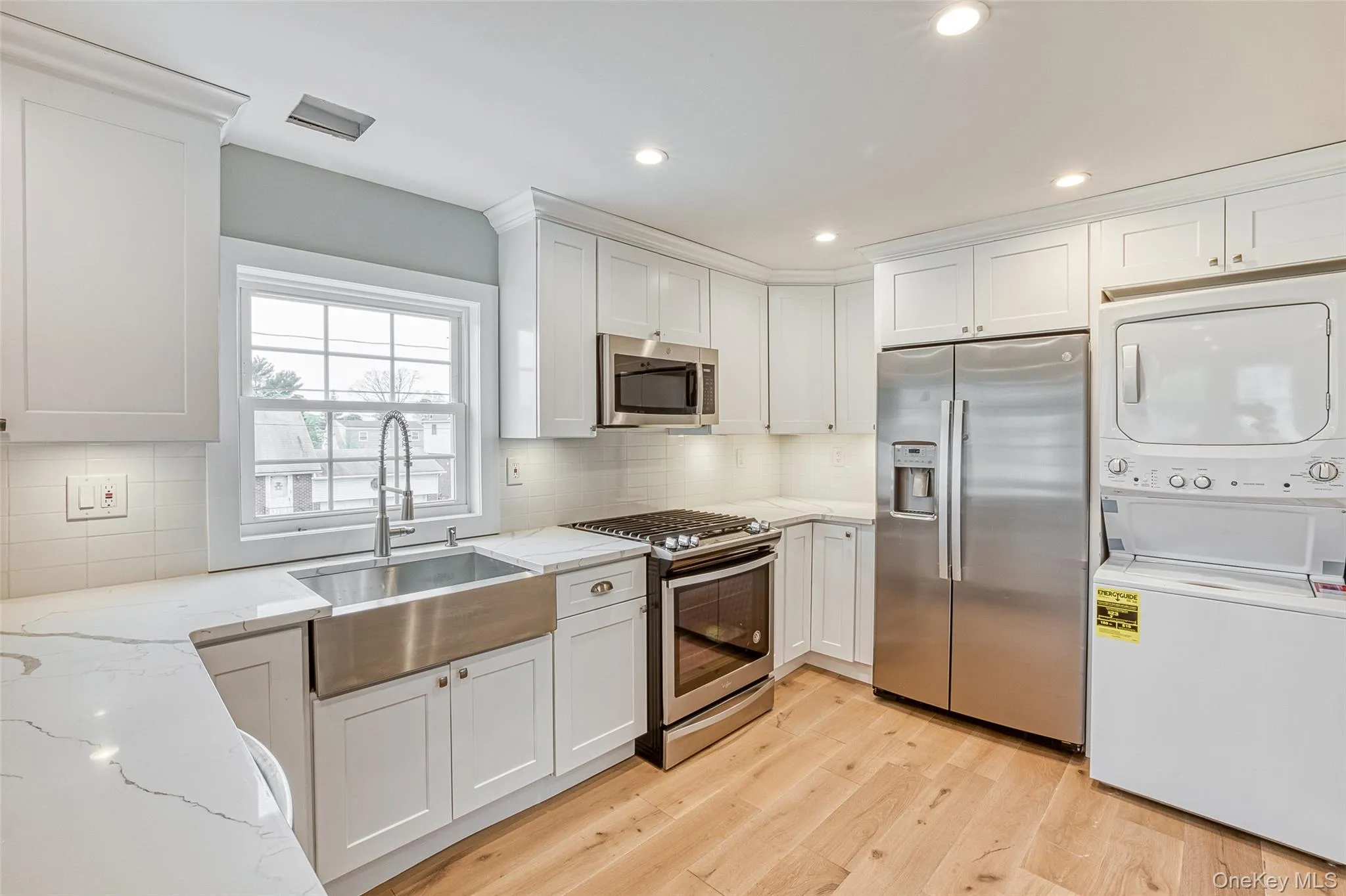 Kitchen featuring stainless steel appliances, light stone countertops, stacked washer / drying machine, white cabinets, and recessed lighting Kitchen featuring stainless steel appliances, light stone countertops, stacked washer / drying machine, white cabinets, and recessed lighting