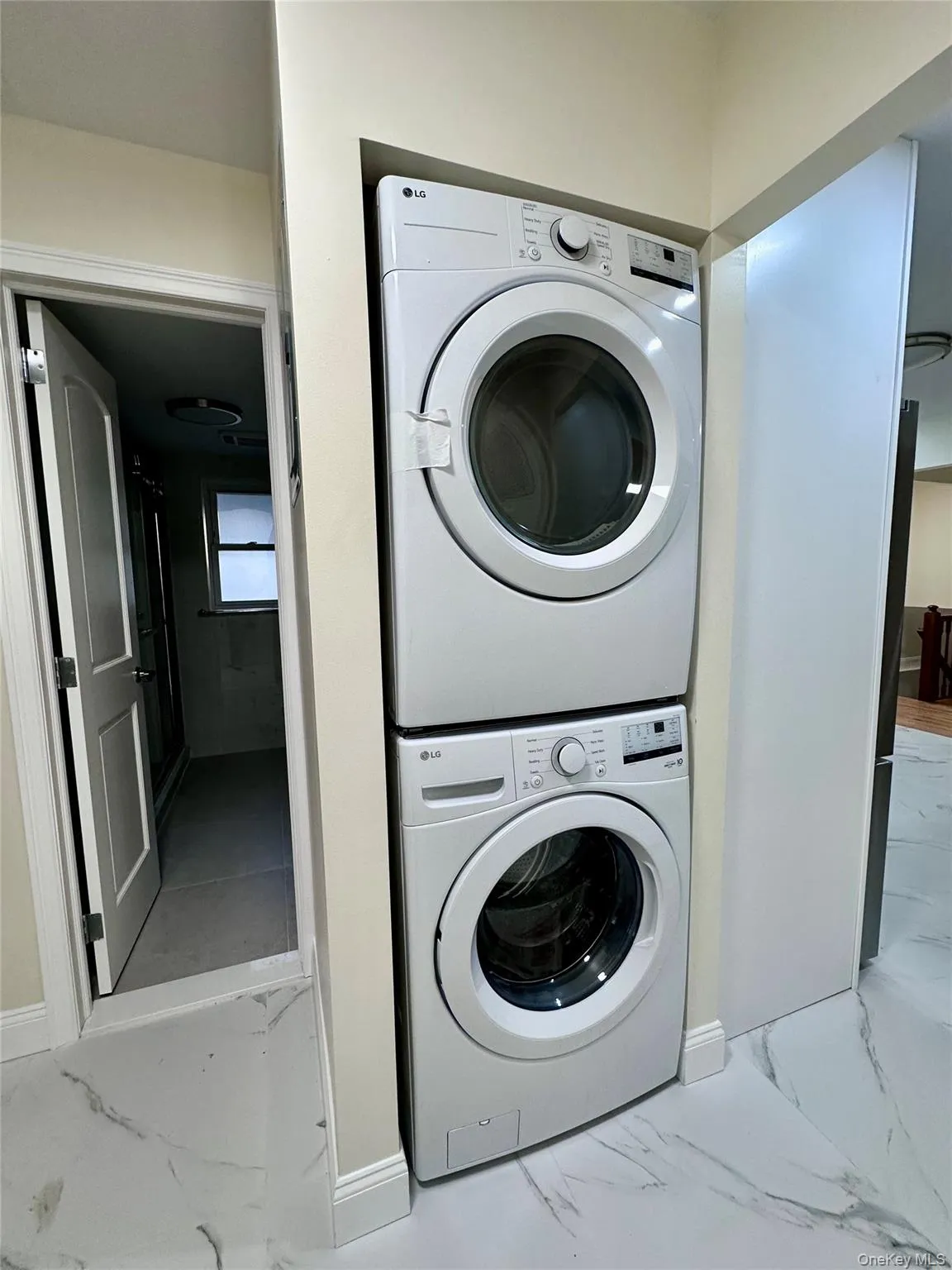 Washroom with light marble finish floors and estacked washer and dryer Washroom with light marble finish floors and estacked washer and dryer