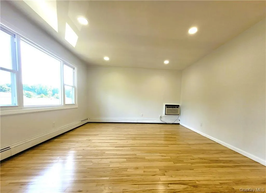 Empty room featuring a baseboard heating unit, light wood-style floors, recessed lighting, and a wall mounted air conditioner Empty room featuring a baseboard heating unit, light wood-style floors, recessed lighting, and a wall mounted air conditioner