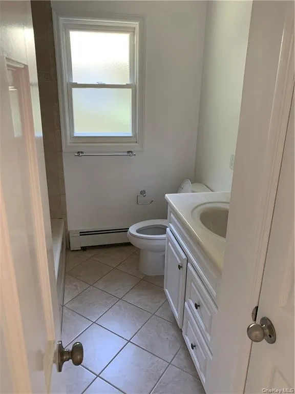 Full bath with vanity, light tile patterned floors, and baseboard heating Full bath with vanity, light tile patterned floors, and baseboard heating