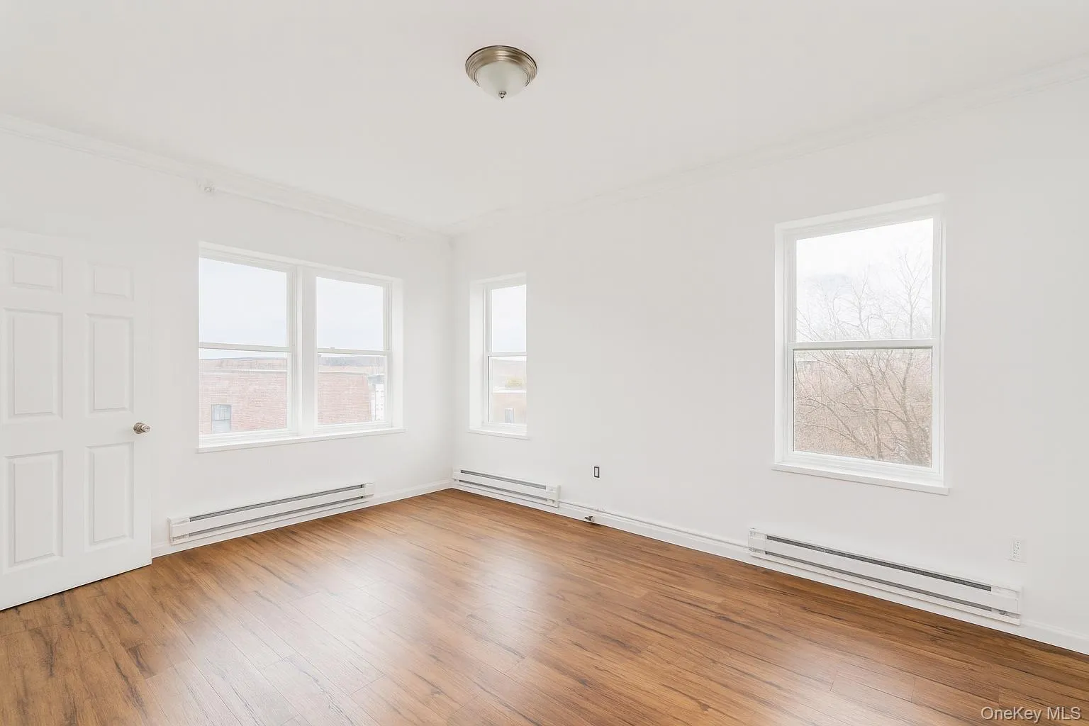 one bedroom with a baseboard heating unit, and light wood-style flooring one bedroom with a baseboard heating unit, and light wood-style flooring