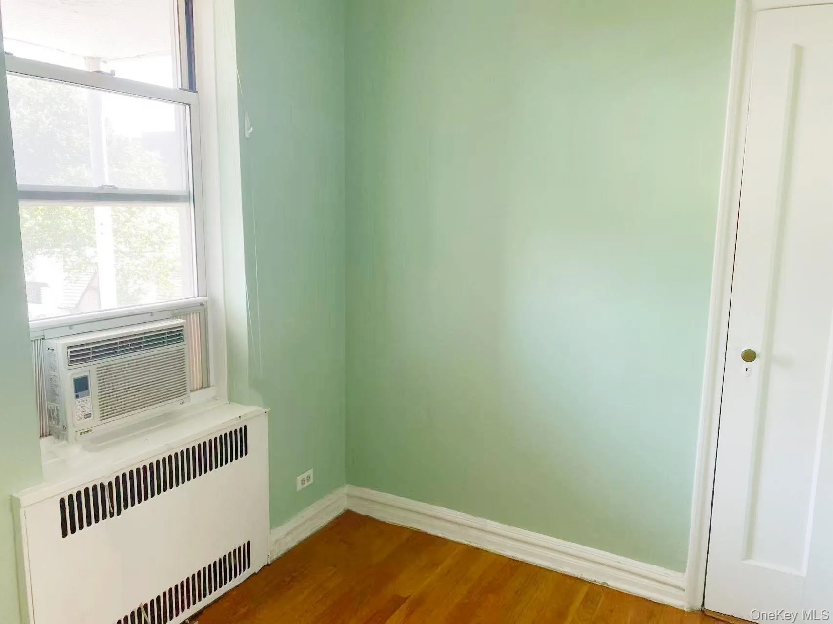 Unfurnished room featuring radiator, plenty of natural light, wood finished floors, and cooling unit Unfurnished room featuring radiator, plenty of natural light, wood finished floors, and cooling unit