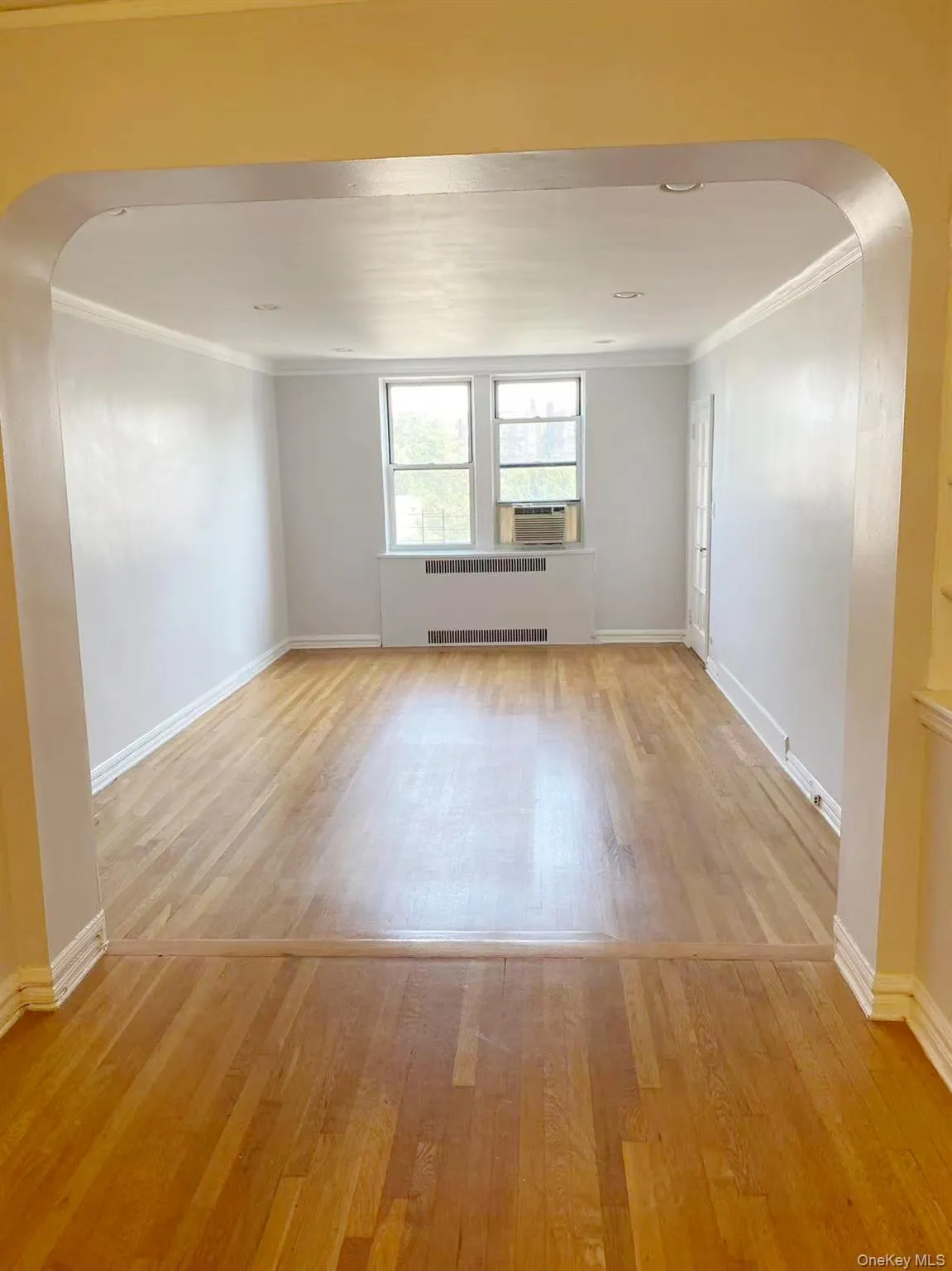 Empty room featuring arched walkways, light wood-style flooring, crown molding, and radiator heating unit Empty room featuring arched walkways, light wood-style flooring, crown molding, and radiator heating unit