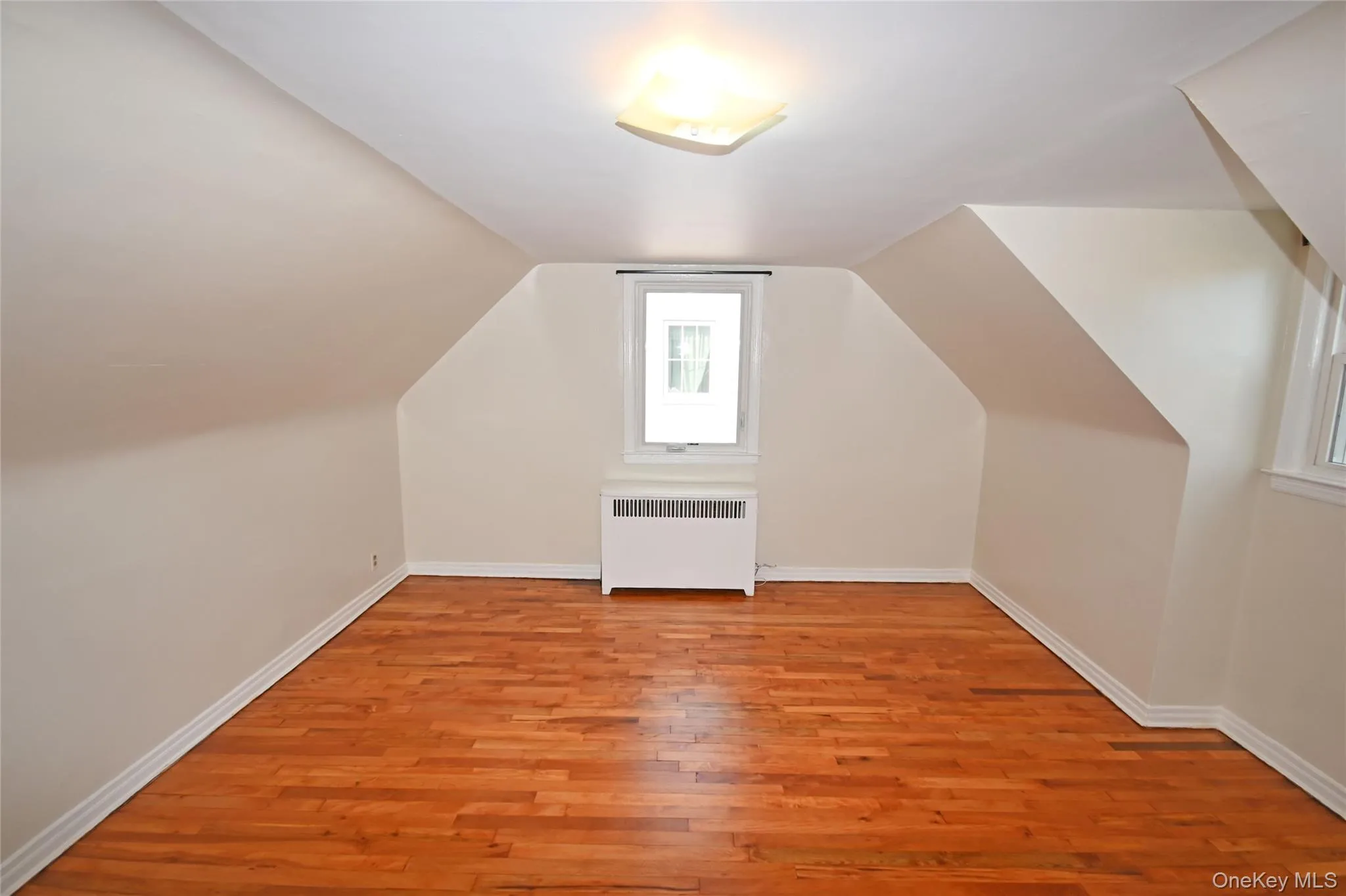 Additional living space with radiator, light wood-style flooring, and vaulted ceiling Additional living space with radiator, light wood-style flooring, and vaulted ceiling