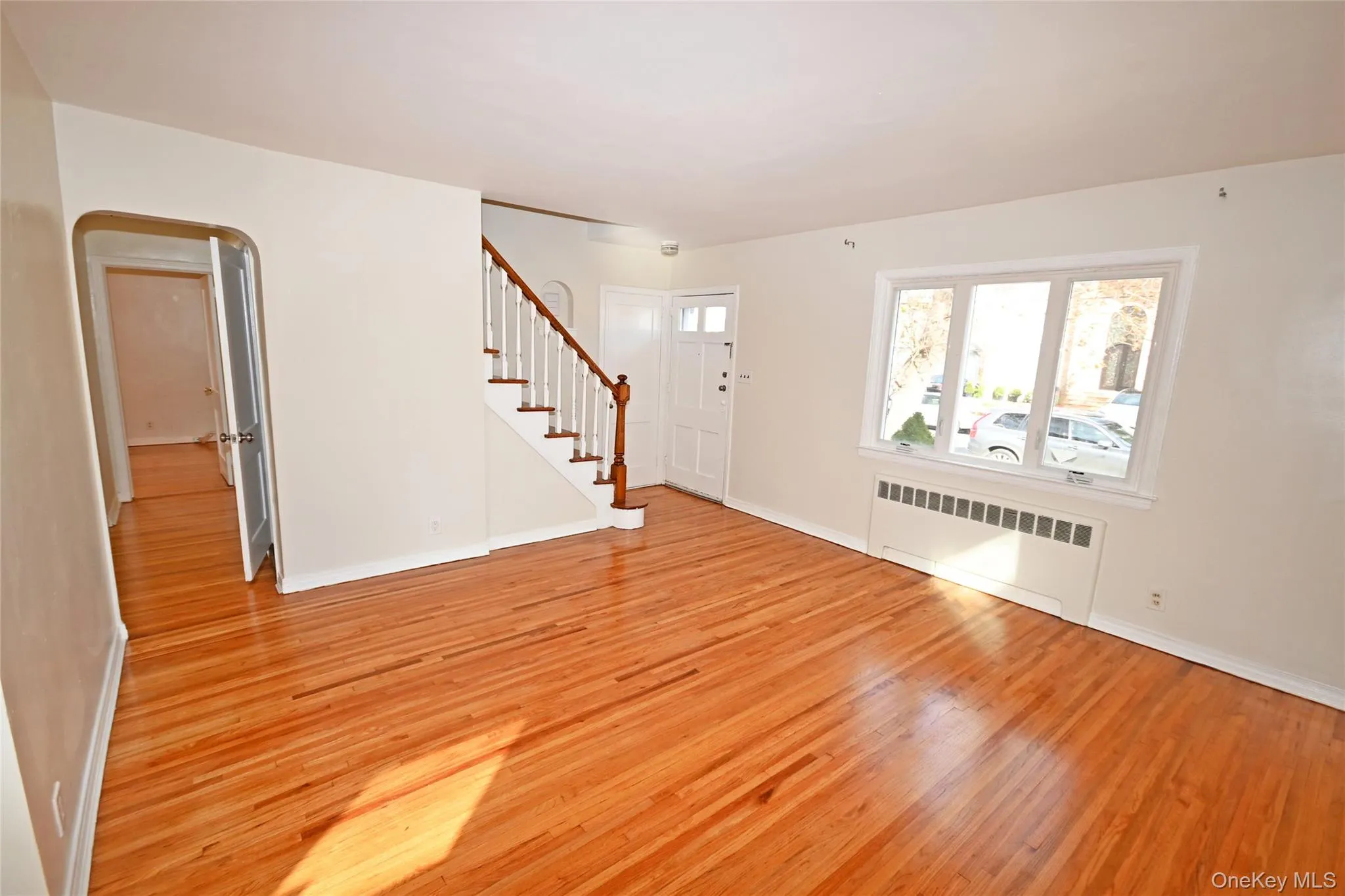 Unfurnished living room featuring radiator, light wood-type flooring, arched walkways, and stairway Unfurnished living room featuring radiator, light wood-type flooring, arched walkways, and stairway